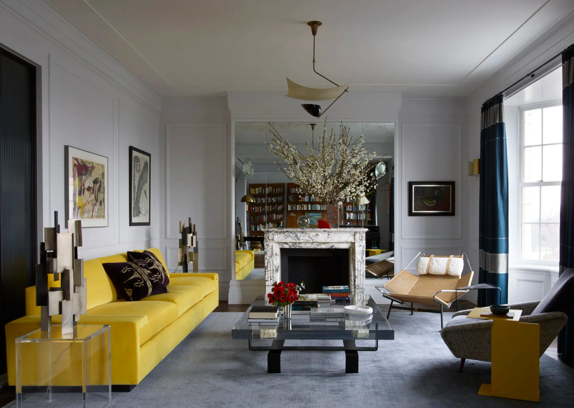 Modern living room with bright yellow sofa, fireplace with white mantel, gray rug, black coffee table, and blue accents throughout, designed by Hannah McKnight.