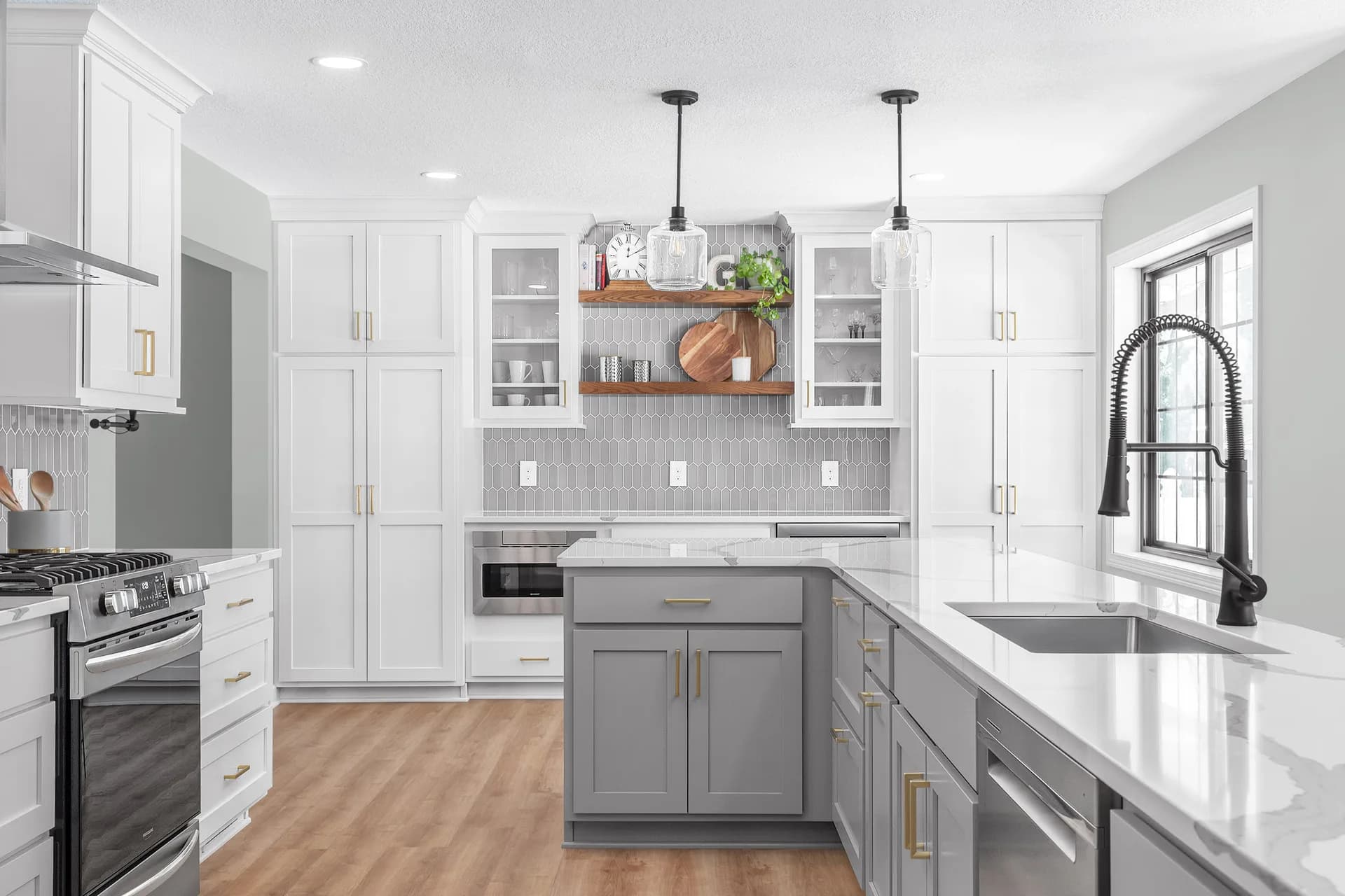Modern kitchen with white cabinetry, gray island, stainless steel appliances, and subway tile backsplash designed by Hayli Tollagson.
