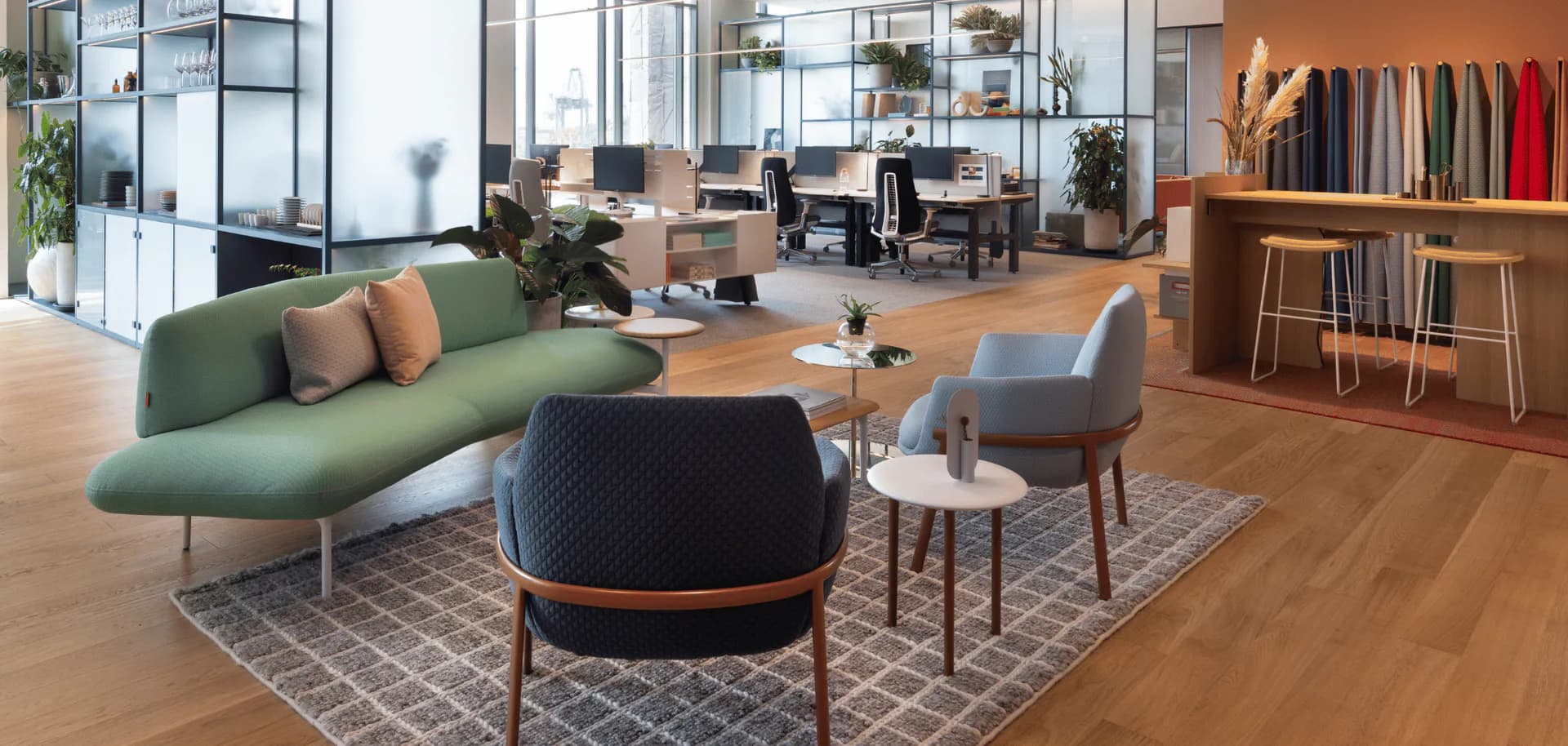Modern office lounge with curved green sofa, black round ottoman, wood flooring, and warm wood shelving by Heather Raho.