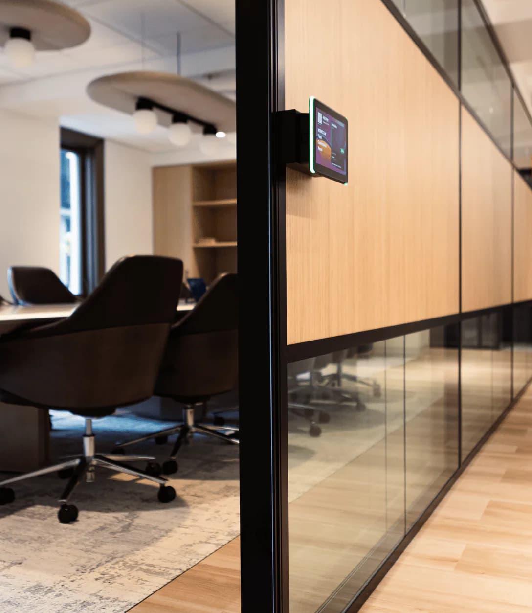 Modern office space with glass partition walls, black frames, light wood paneling, black office chairs, and recessed ceiling details by Heather Raho.