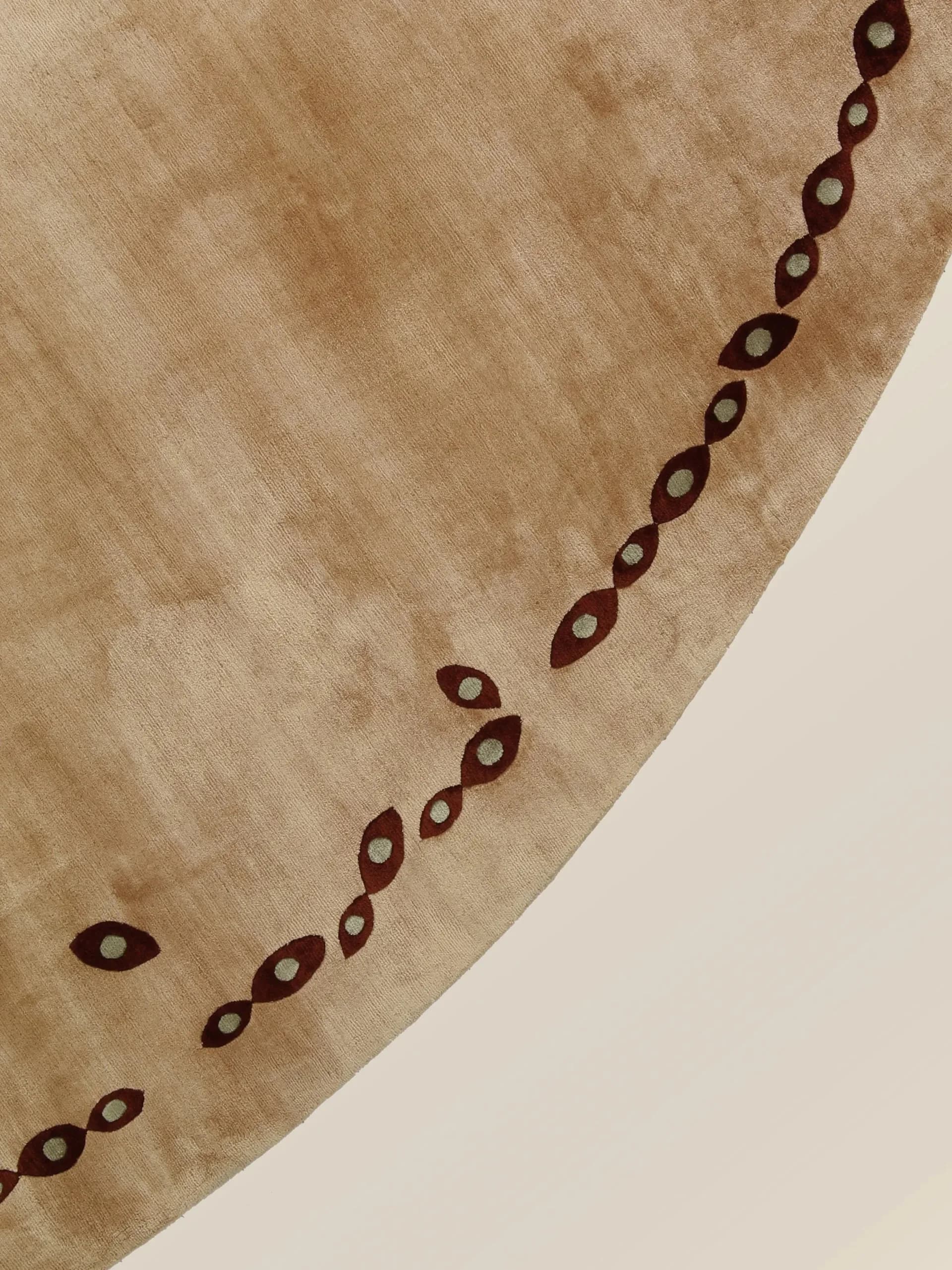 Curved textile or surface detail featuring a chain of dark burgundy eye-shaped motifs arranged in a diagonal pattern on natural linen by Hillary Petrie.