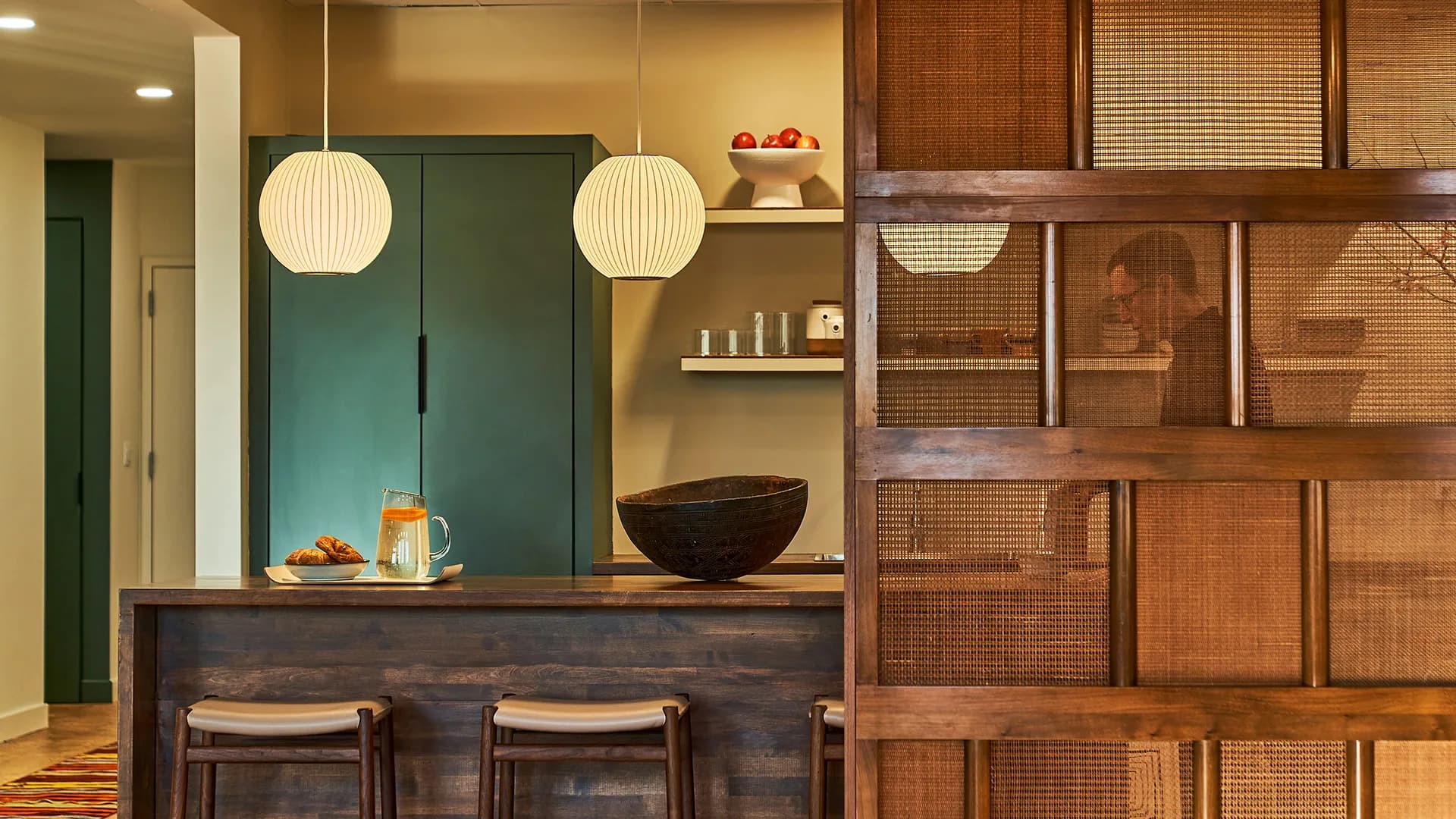 Modern kitchen with dark wood cabinetry, teal green upper cabinets, pendant lighting, and rattan-fronted storage by Hines Fischer.