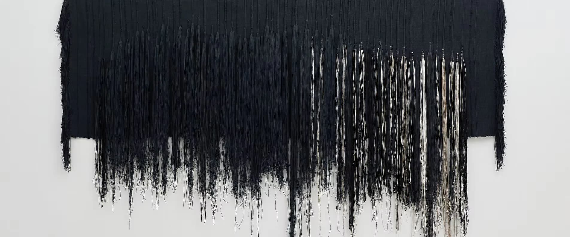Black fringe installation with gradient effect transitioning from dense to sparse strands, creating a textured sculptural wall piece by Hiroko Takeda.