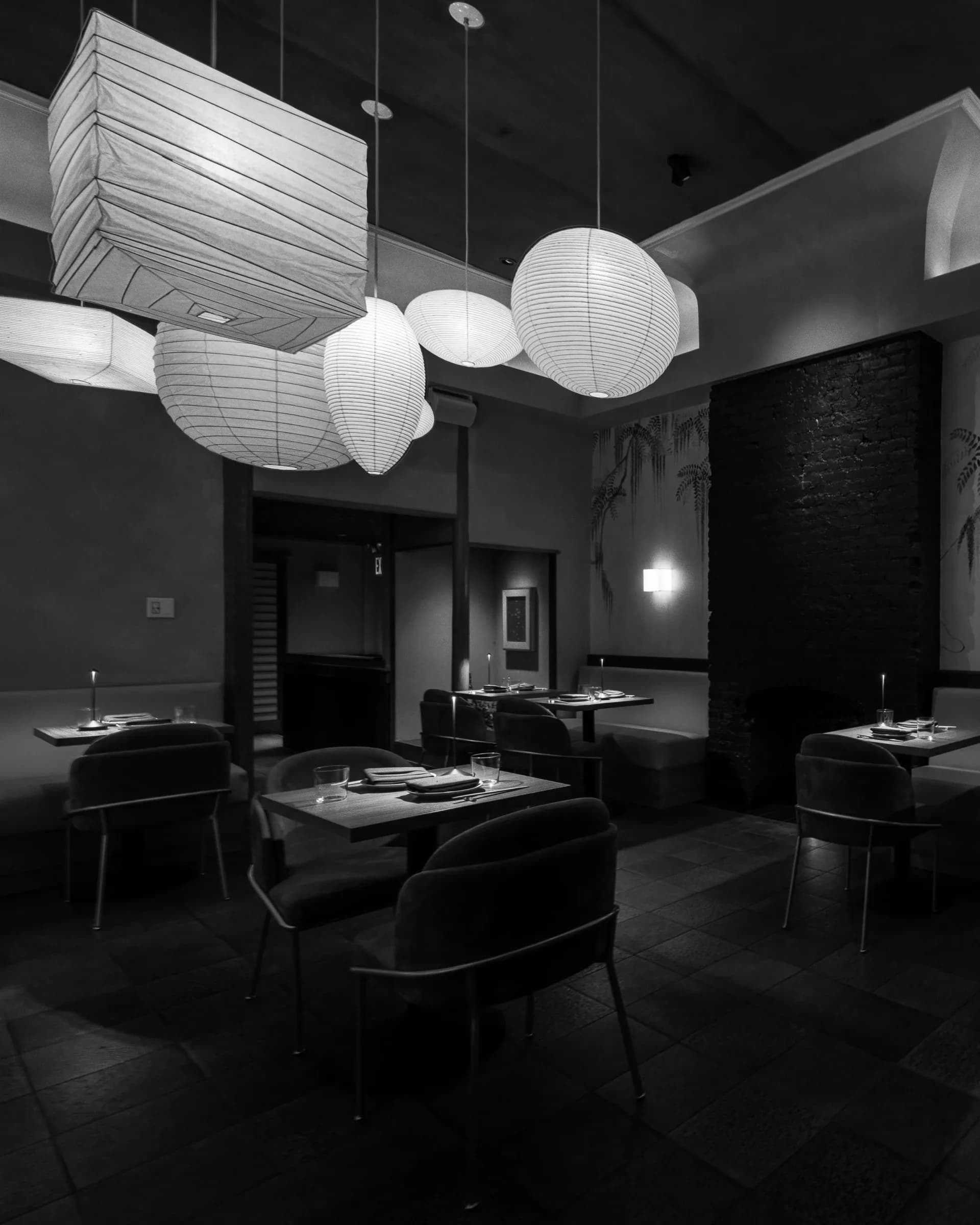 Modern black restaurant interior with white paper pendant lights, dark furnishings, and minimalist place settings designed by Ian Bentley.