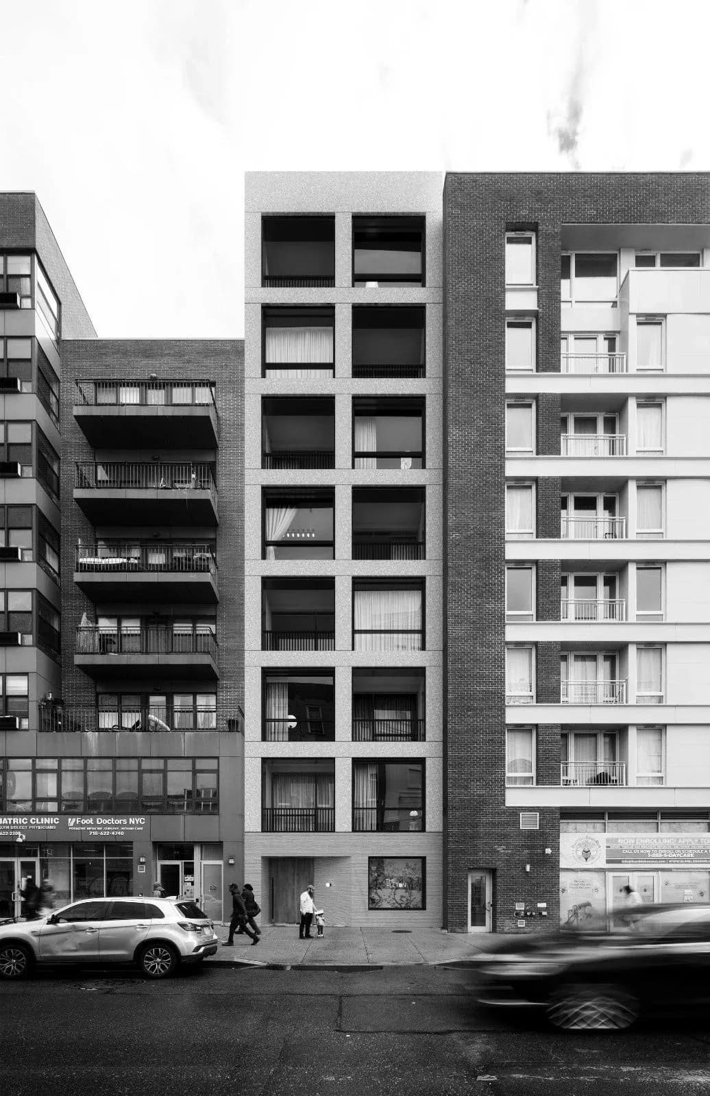 Modernist residential building facade with regular grid of windows in brick and light stone, street-level retail, parked cars below by Ian Bentley.