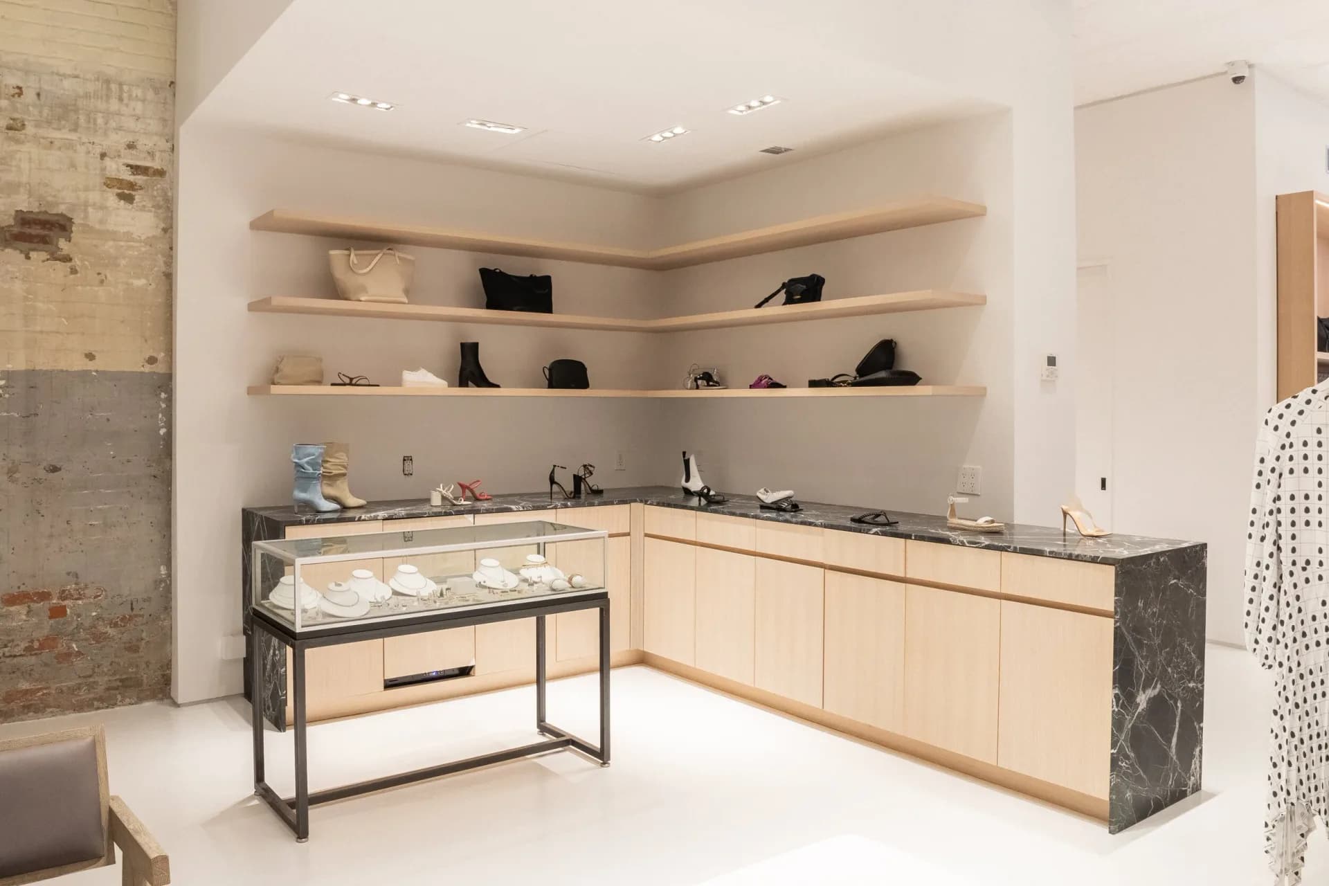 Luxury jewelry retail interior with light wood cabinetry, floating shelves, display cases, and marble accent walls by Ian Carrington.