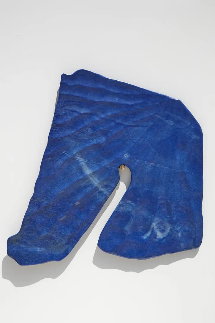 Deep blue sculptural stone or mineral form with organic curved surfaces and a white cylindrical element, displayed against a neutral background by Ian Collings.