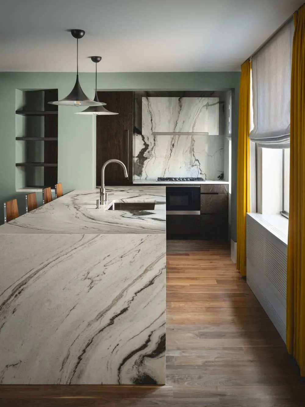 Modern kitchen with curved marble island, black cabinetry, and sage green walls, designed by Inga Oren.