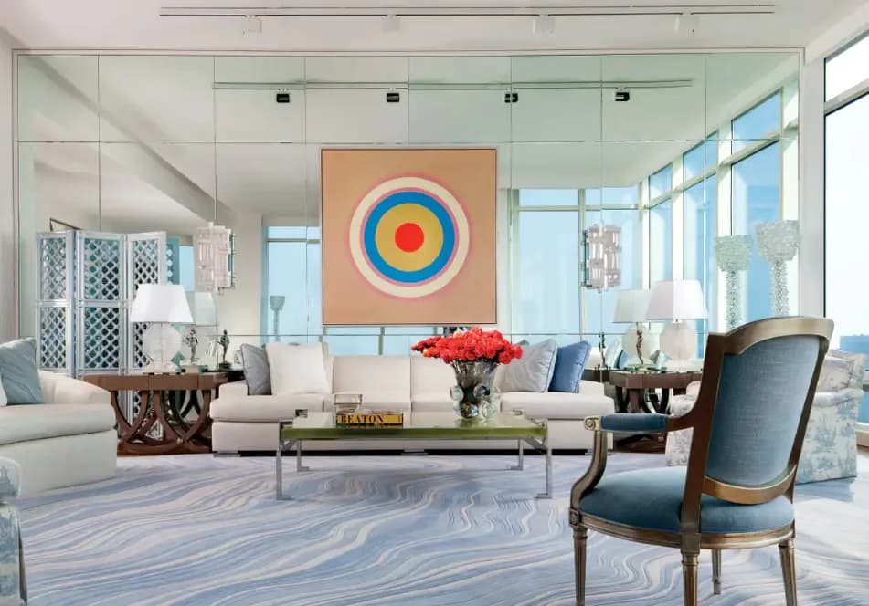 Bright modern living room with white seating, blue accent chair, colorful target artwork, and expansive windows overlooking the city by Ingrid Garbar.