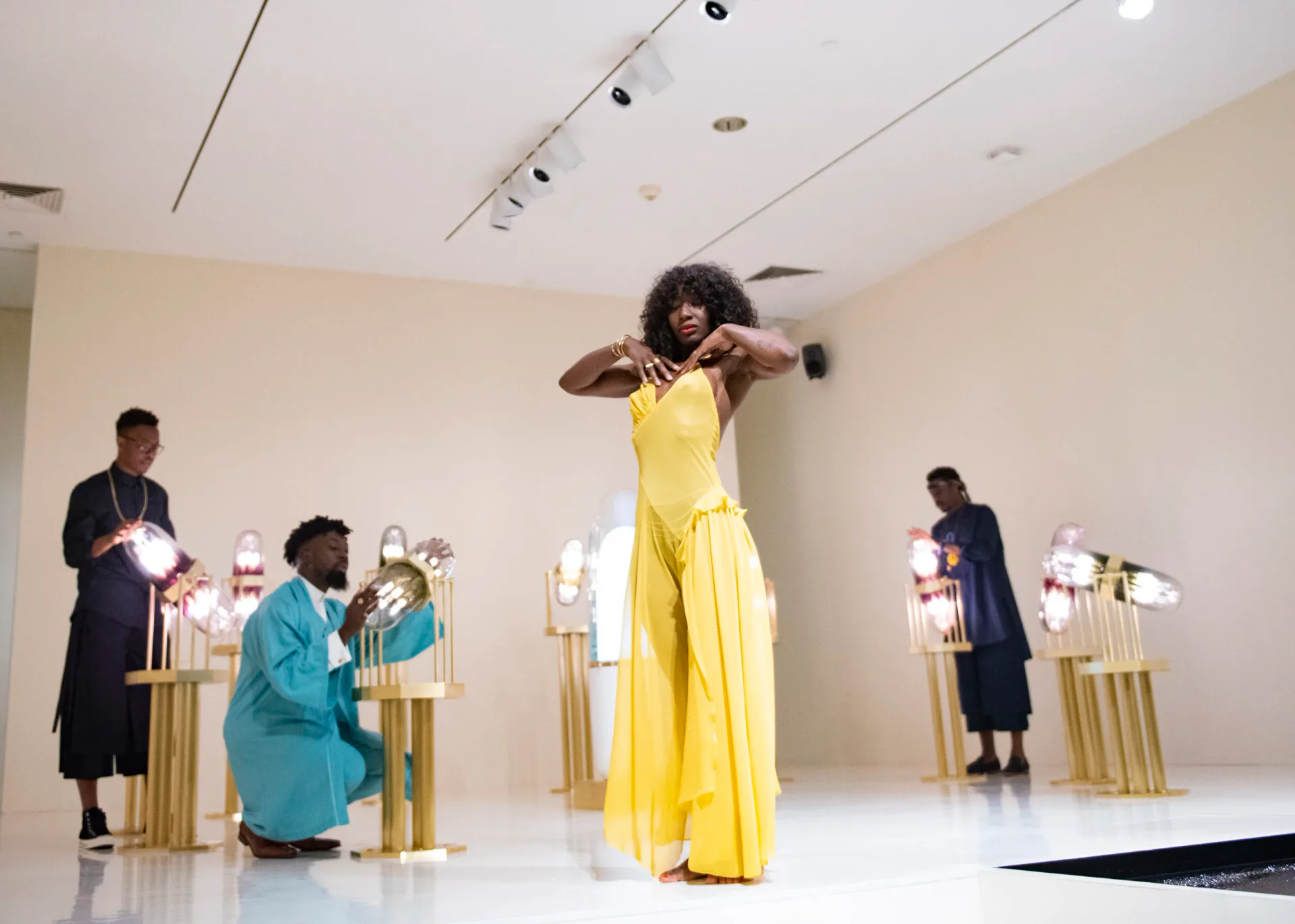 Modern exhibition space with cream walls and gold cylindrical pedestals displaying sculptural pieces, designed by Ini Archibong.