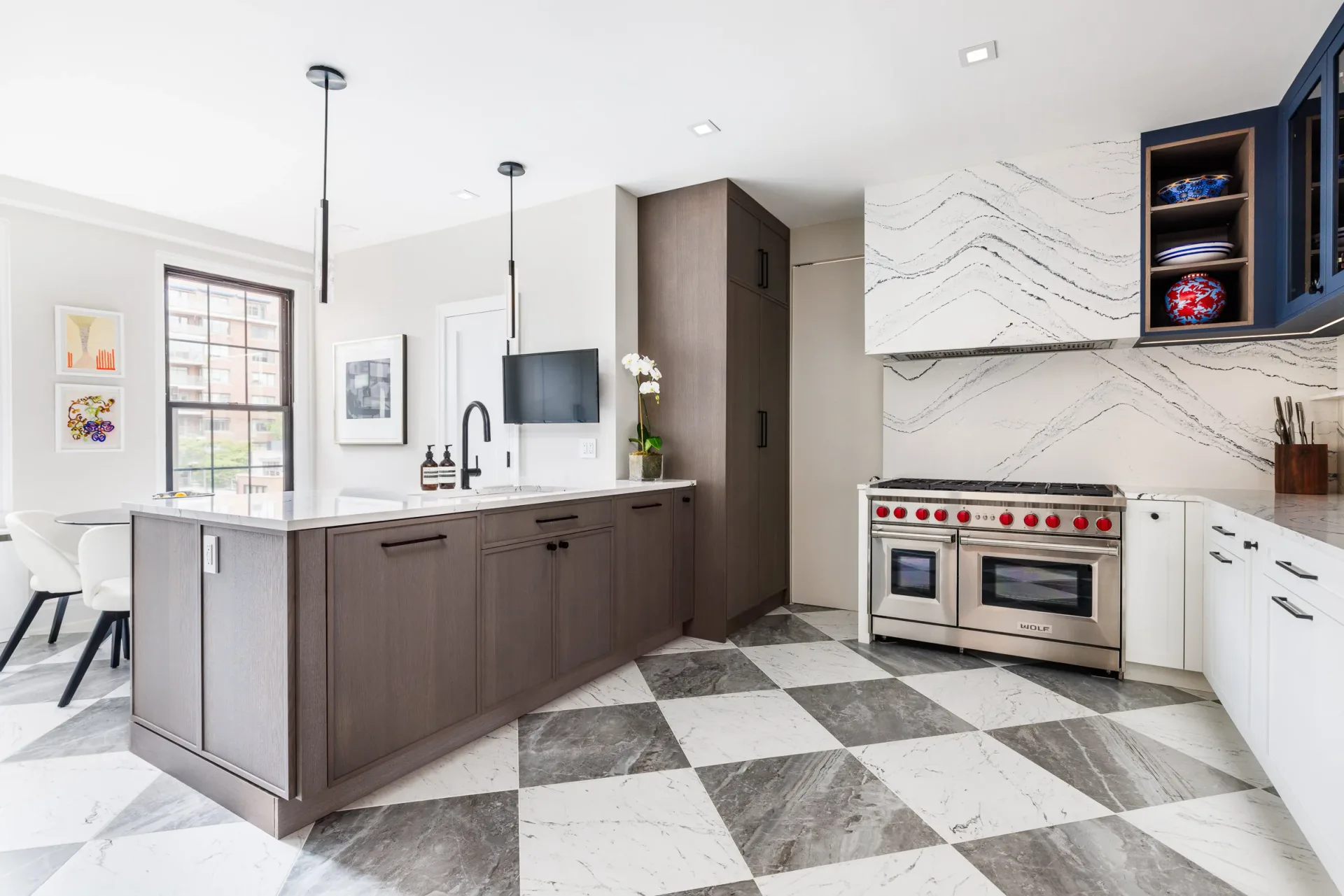 Contemporary kitchen with dark brown cabinetry, white marble countertops, geometric black and white floor tiles, stainless steel range, and pendant lighting by Ipek Kaypak.