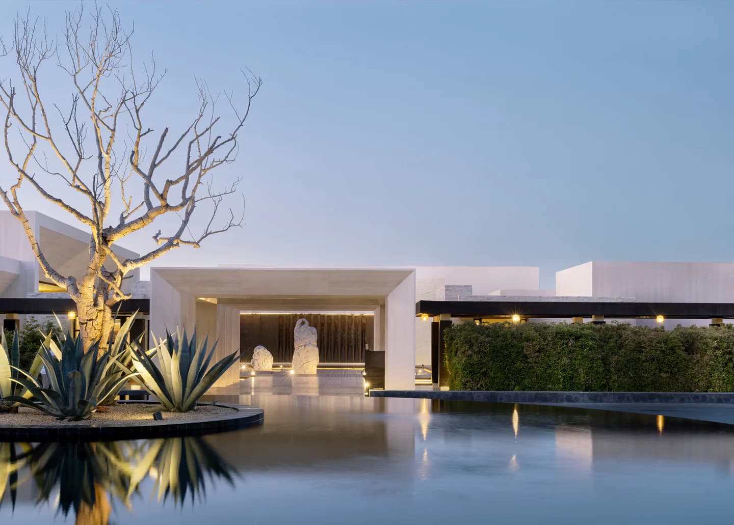 Minimalist luxury courtyard with reflective water surface, golden-lit sculptural tree, white modernist architecture, and manicured hedges by Isaac Jimenez.