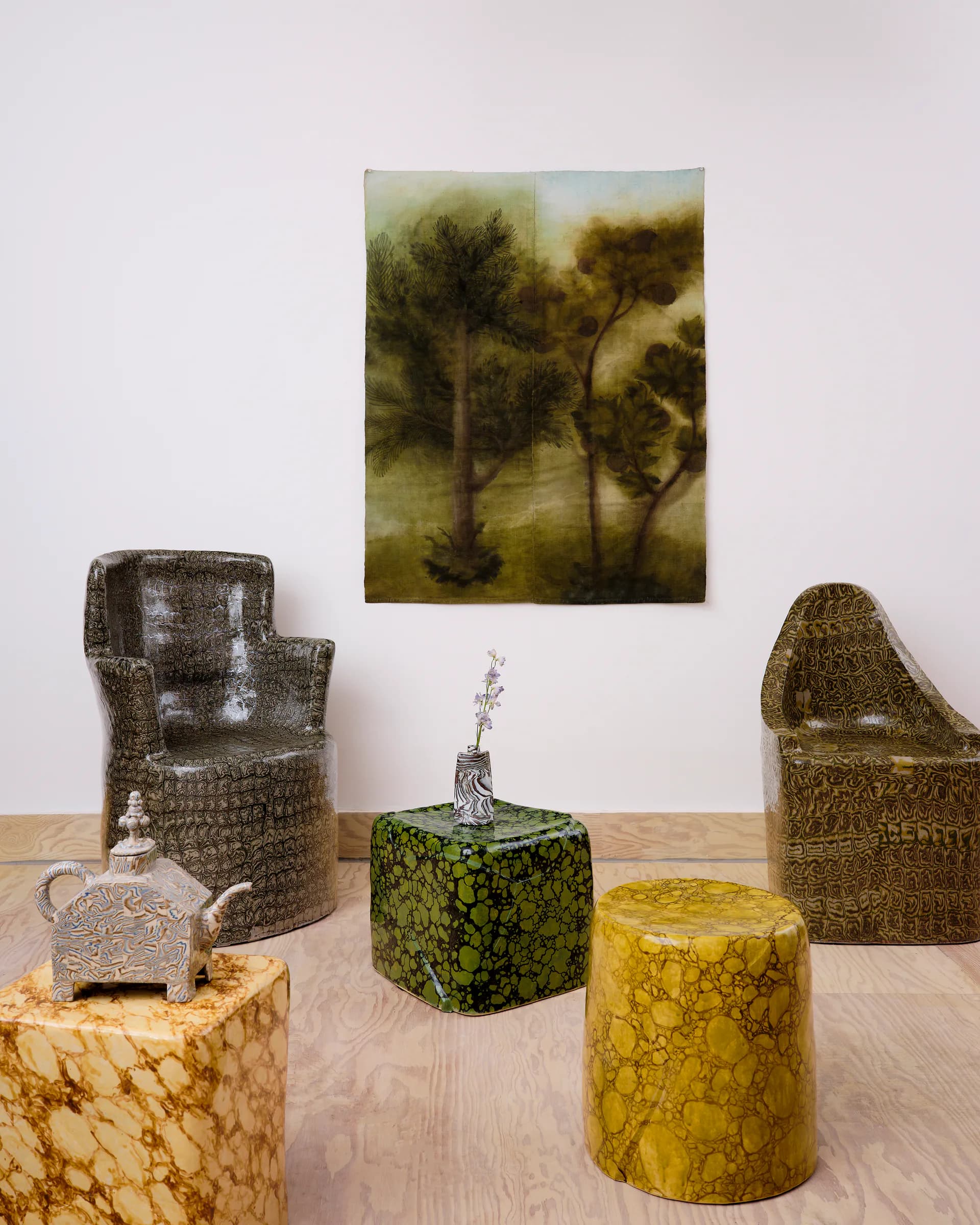 Styled interior vignette featuring textured seating, patterned cylindrical stools, and a landscape artwork in muted earth tones by Isabel Rower.