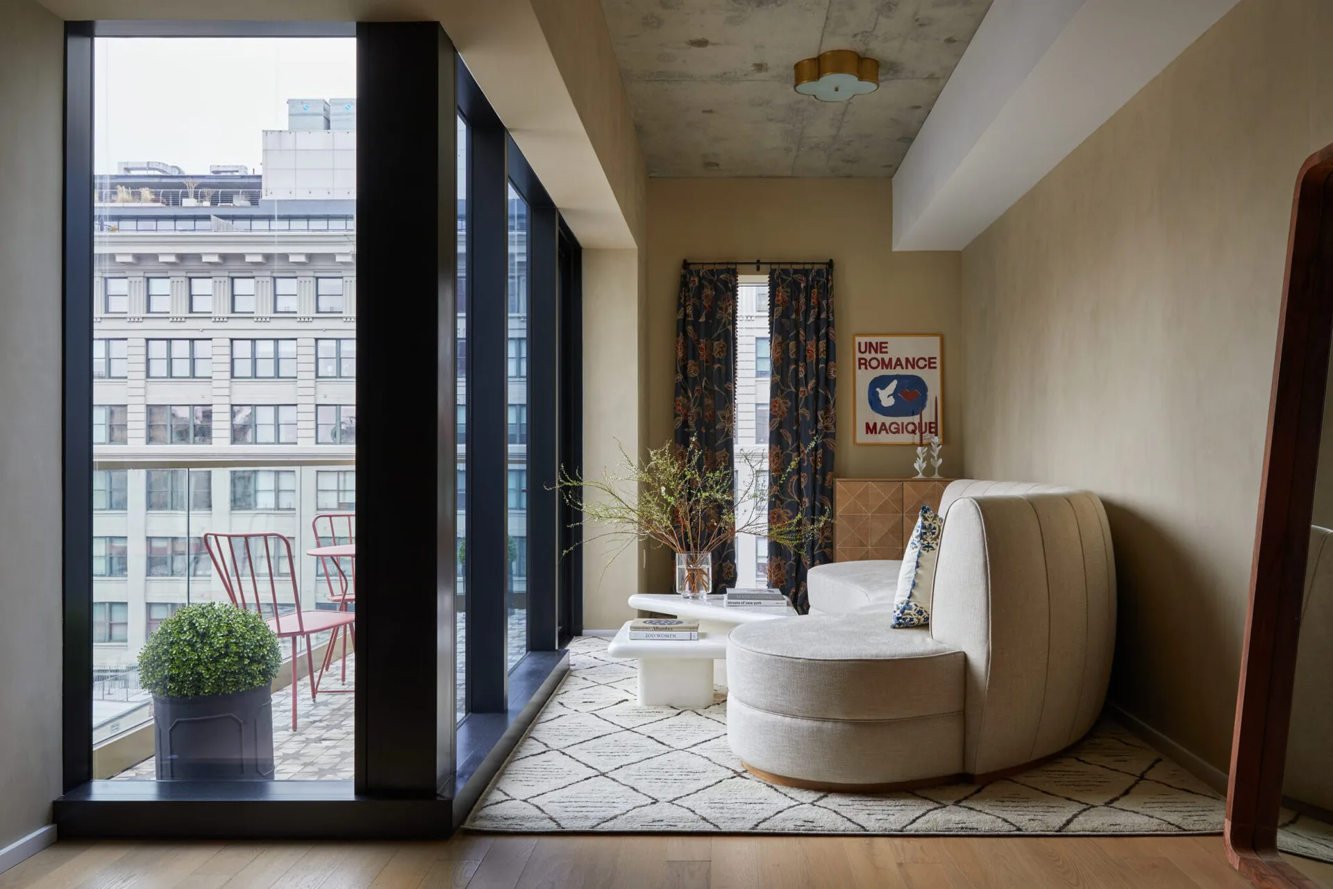 Modern residential interior with curved cream furniture, expansive city views through floor-to-ceiling windows, geometric patterned flooring, and minimalist décor by Isabel Runsewe.