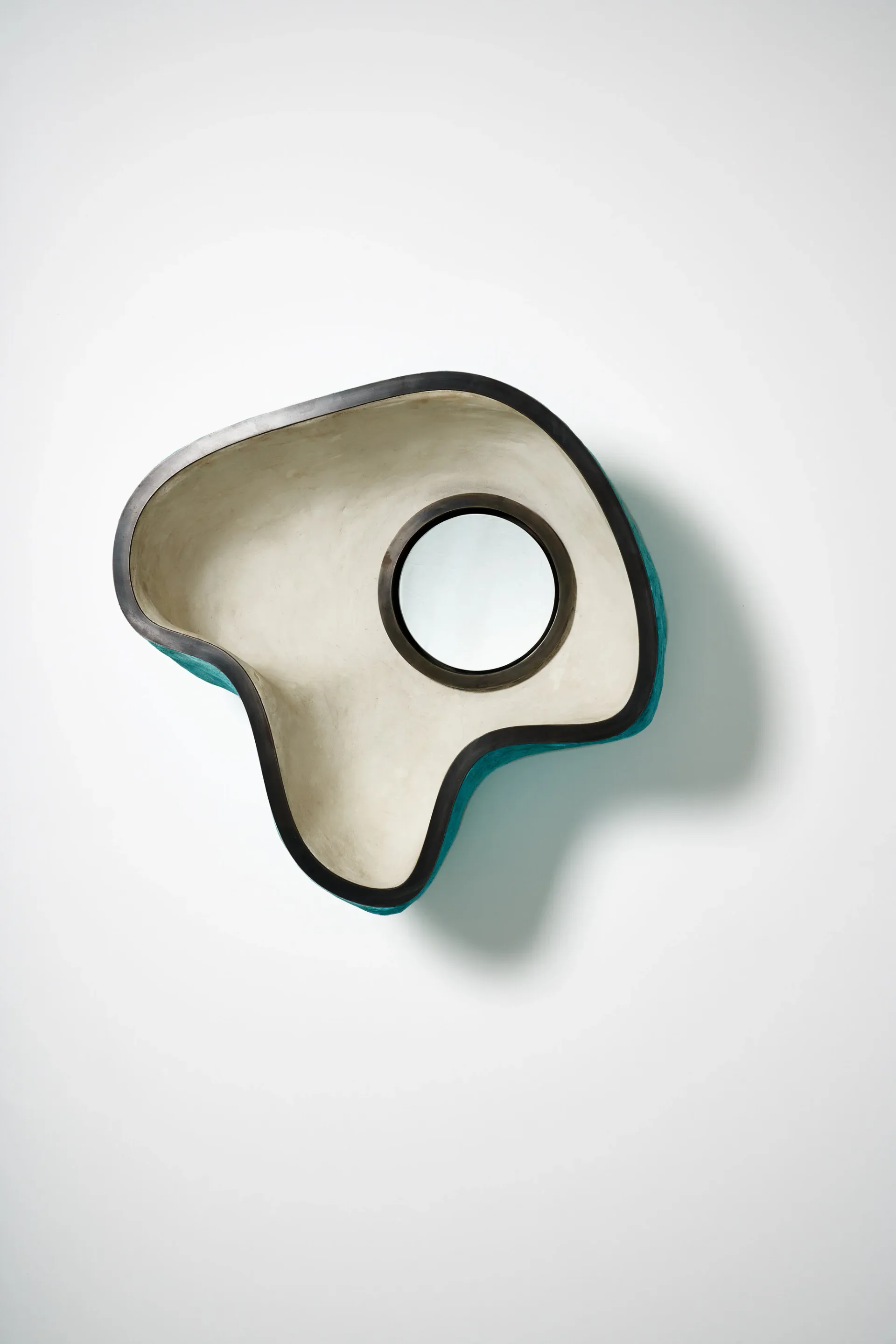 Abstract sculptural bowl form in cream and teal with circular aperture, photographed against white background, by J McDonald.
