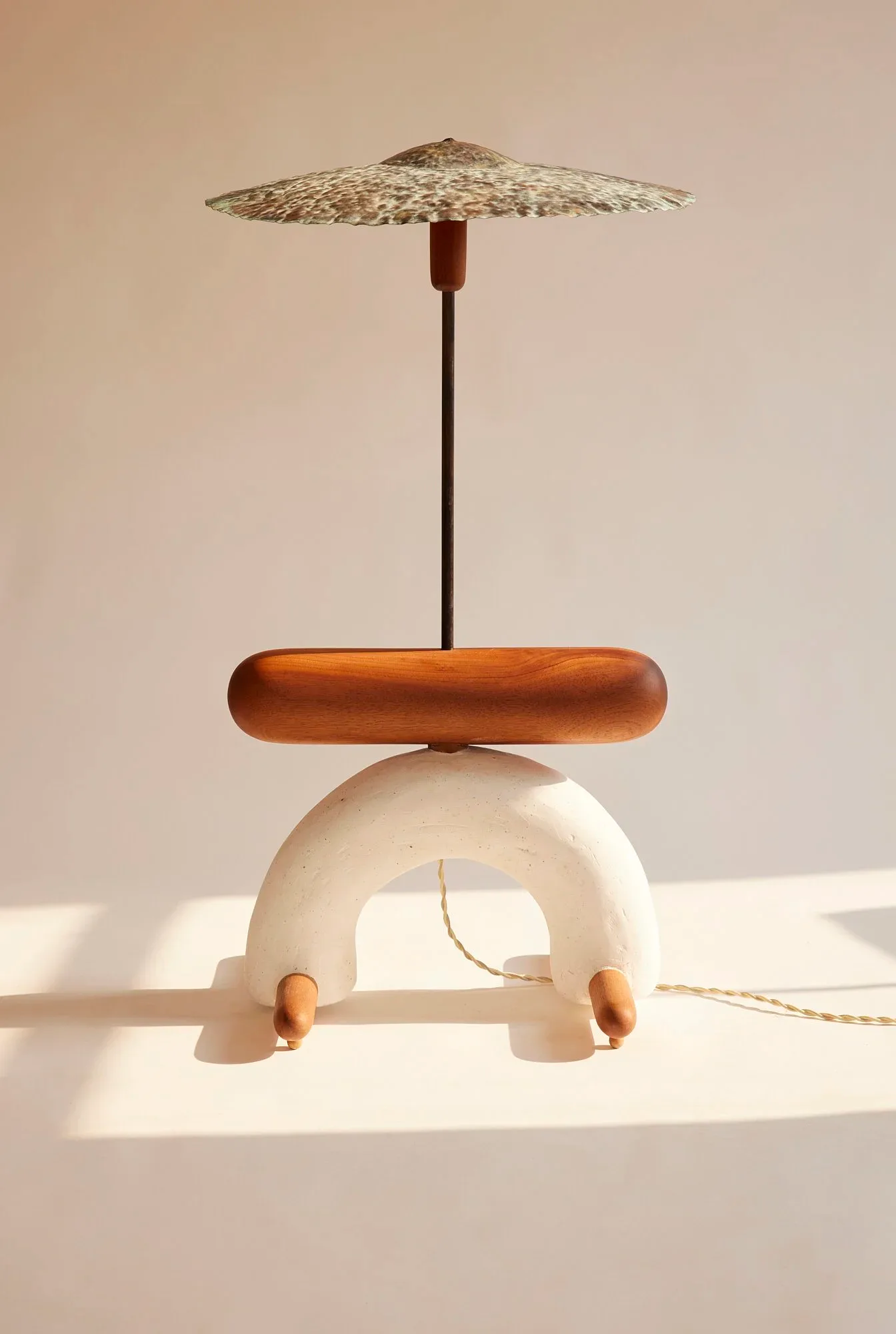 Sculptural table lamp with cream arch base, wooden bowl-shaped tray, dark metal stem, and woven natural fiber shade by Jackrabbit Studio.