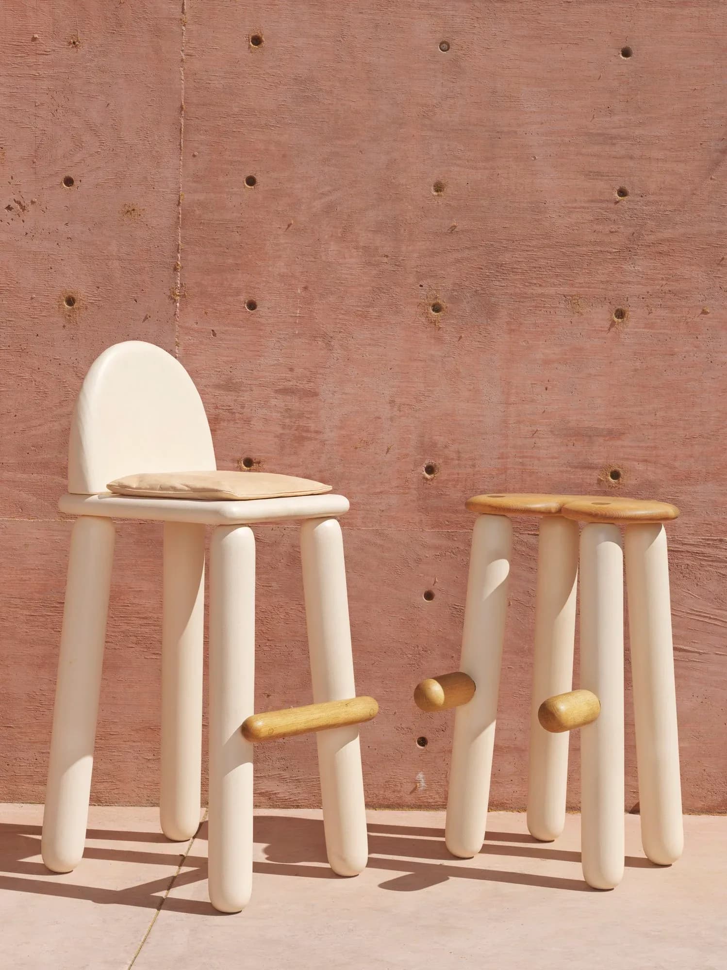 Cream-colored cylindrical furniture pieces with brass accents arranged against a terracotta brick wall with metal fasteners, by Jackrabbit Studio.