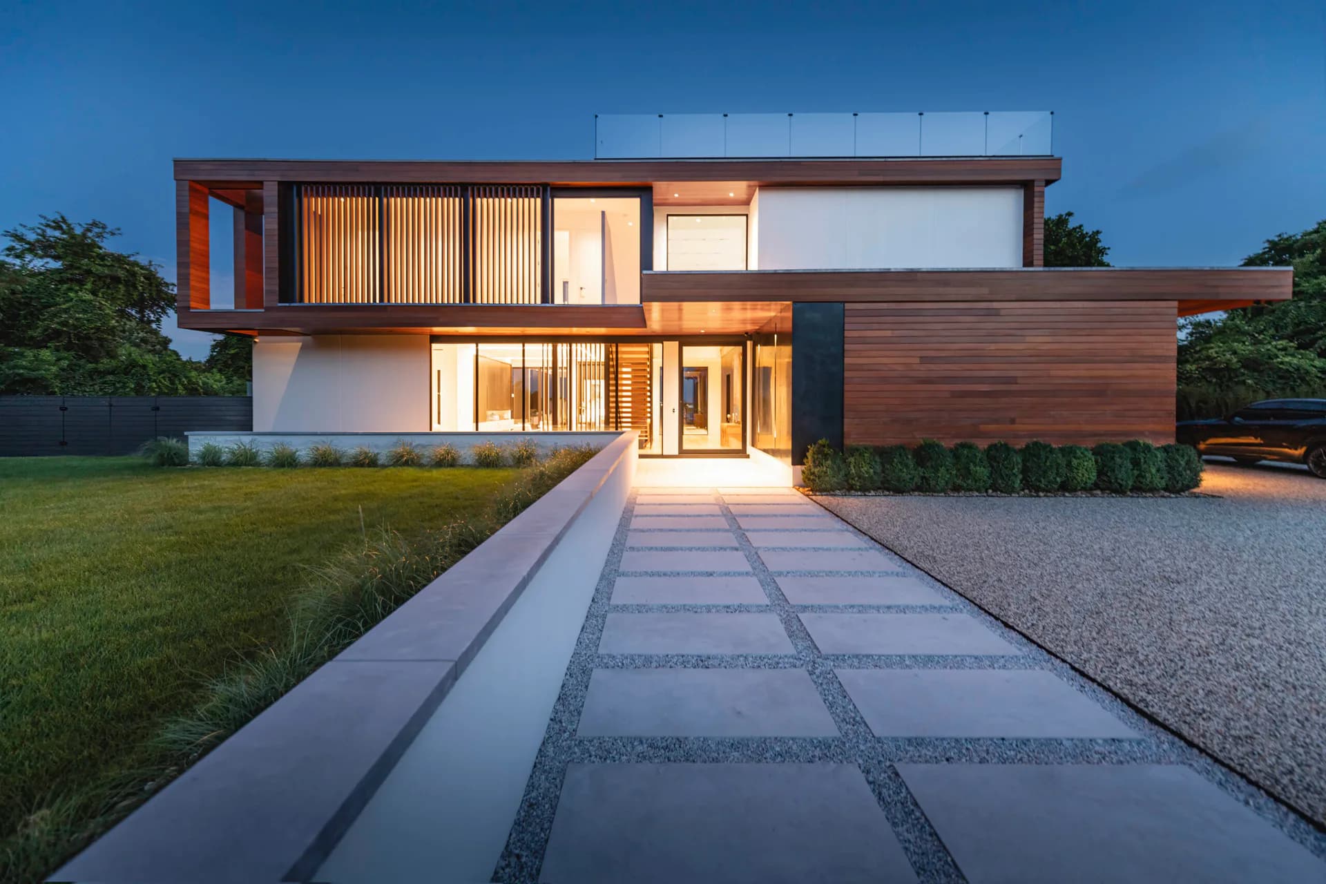 Modern residential house with cantilevered volumes, warm wood cladding, and illuminated interior at dusk, designed by Jaclyn Letsch.
