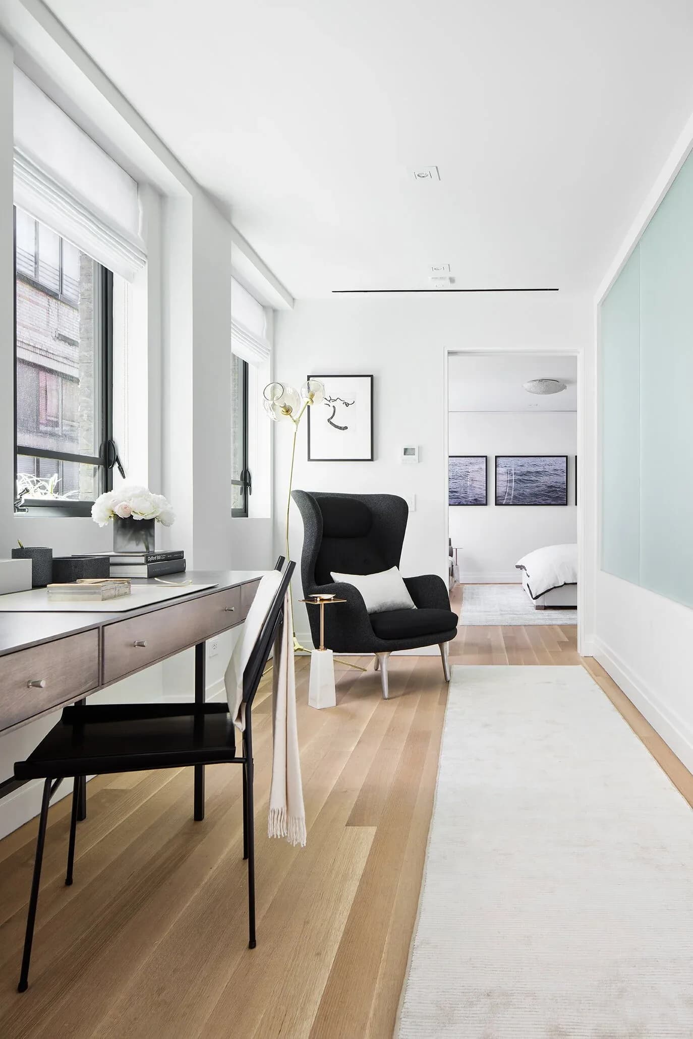 Minimalist home office with light wood flooring, black furniture, white walls, and a pale blue accent wall, designed by Jacqueline Nguyen.