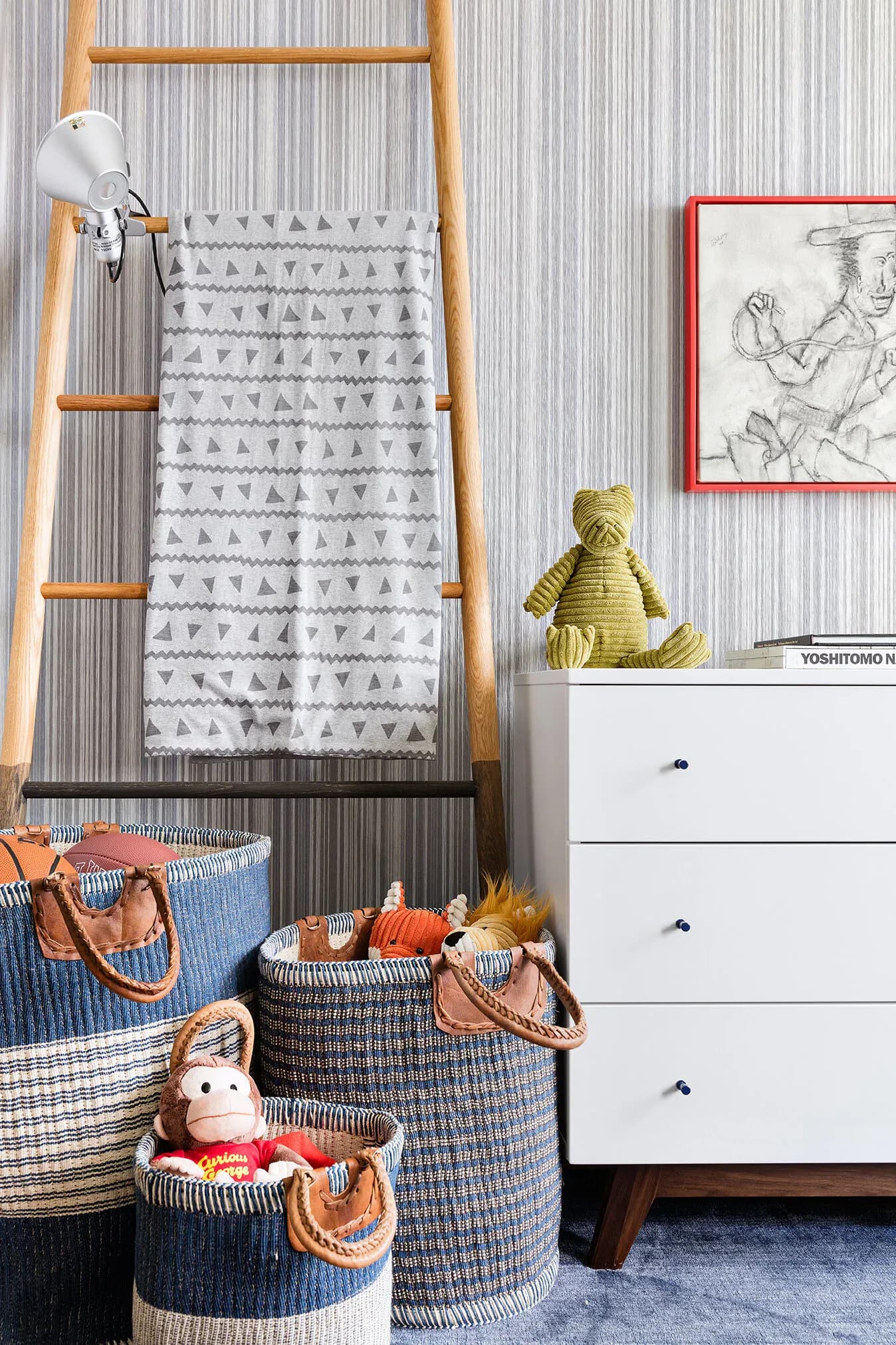 Nursery interior with wooden ladder, woven storage baskets, white dresser, and corrugated metal accent wall in neutral tones by Jacqueline Nguyen.