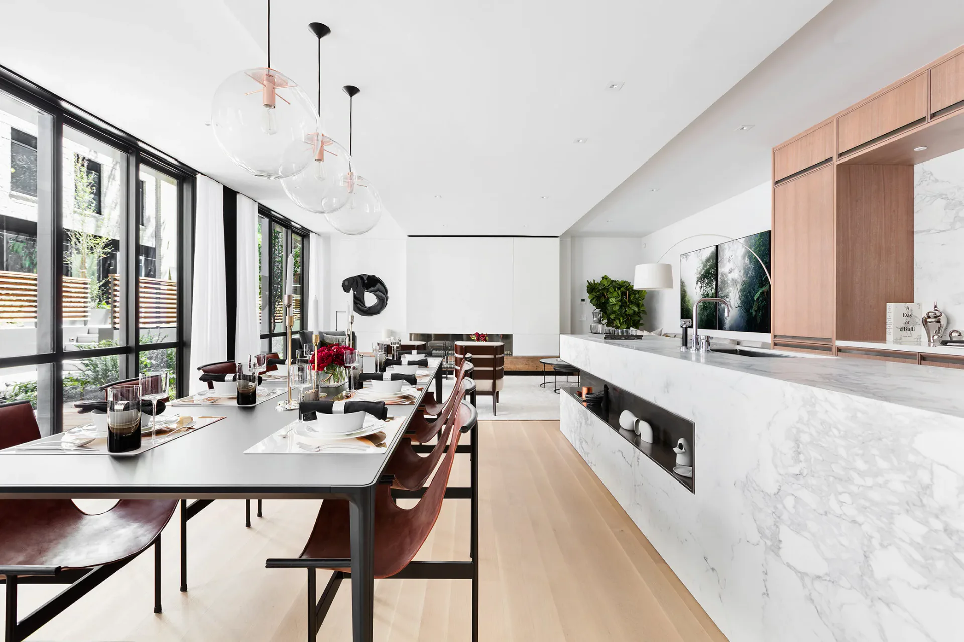 Modern kitchen and dining space with marble countertops, wood cabinetry, minimalist pendant lighting, and natural wood flooring by Jacqueline Nguyen.