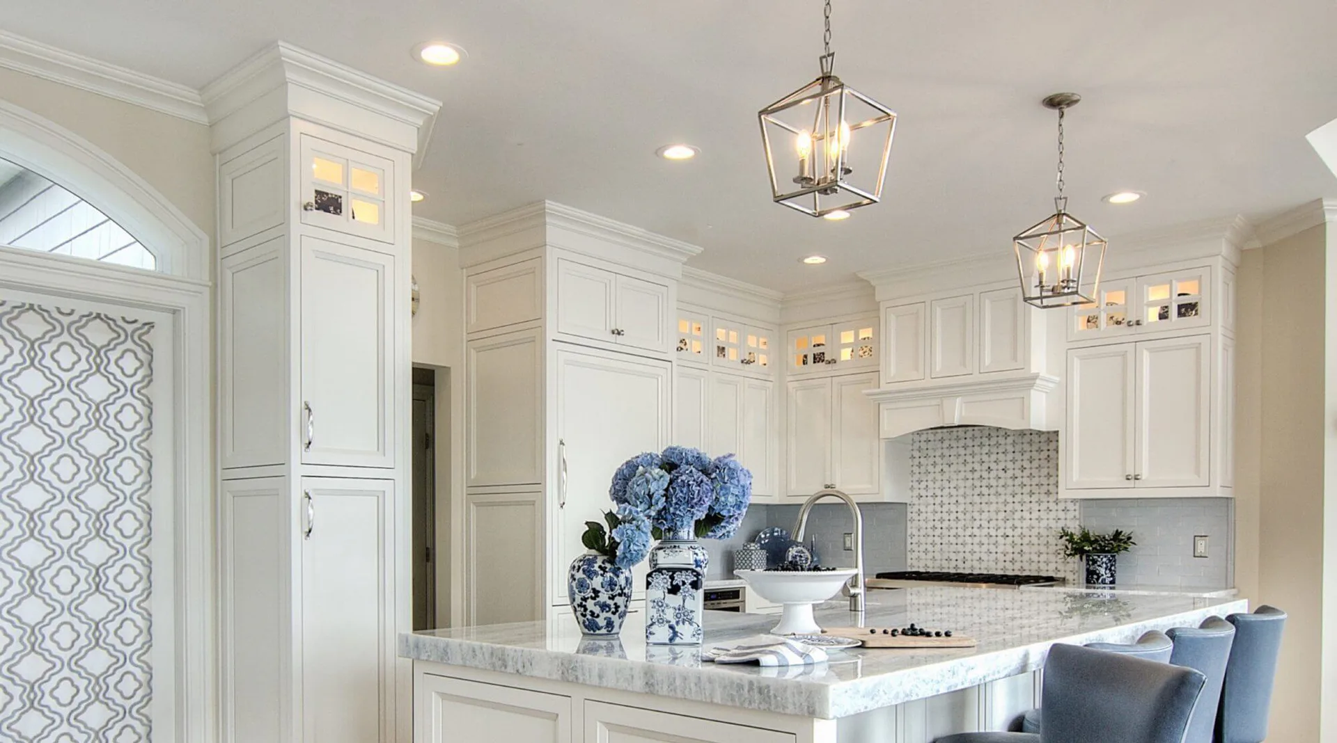 Bright, modern kitchen with white cabinetry, marble countertops, blue-toned backsplash, and coordinating bar seating by Jacquelyn Lagravinese.
