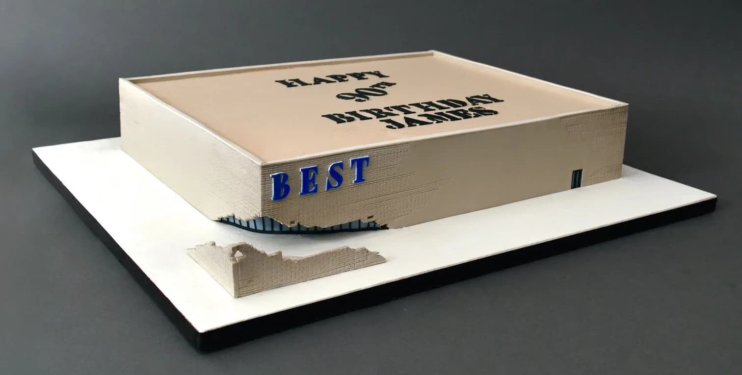Architectural model with cream-colored cardboard box featuring blue branding and white base platform, demonstrating packaging design by James Wines.