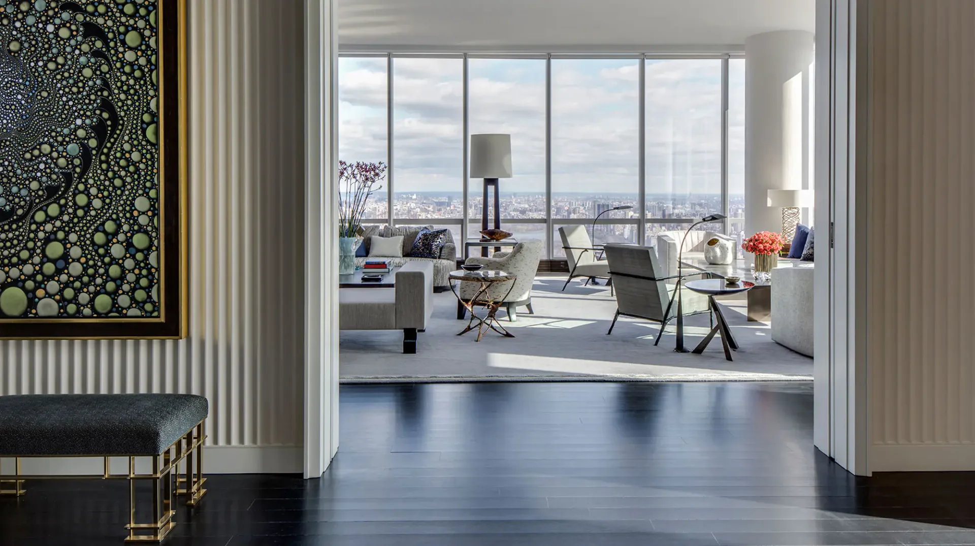 Modern high-rise office with floor-to-ceiling windows, minimalist furniture, polished dark flooring, and city skyline views, designed by Jamie Drake.