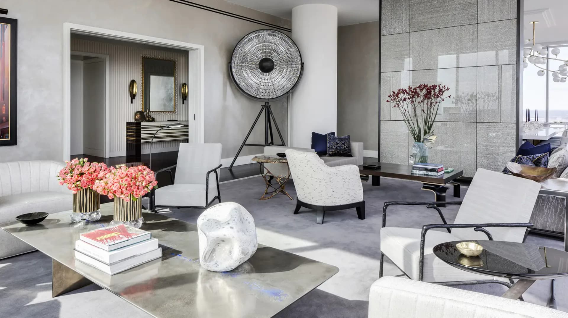 A modern living room with neutral palette featuring white seating, marble coffee table, coral flowers, and sculptural accessories by Jamie Drake.