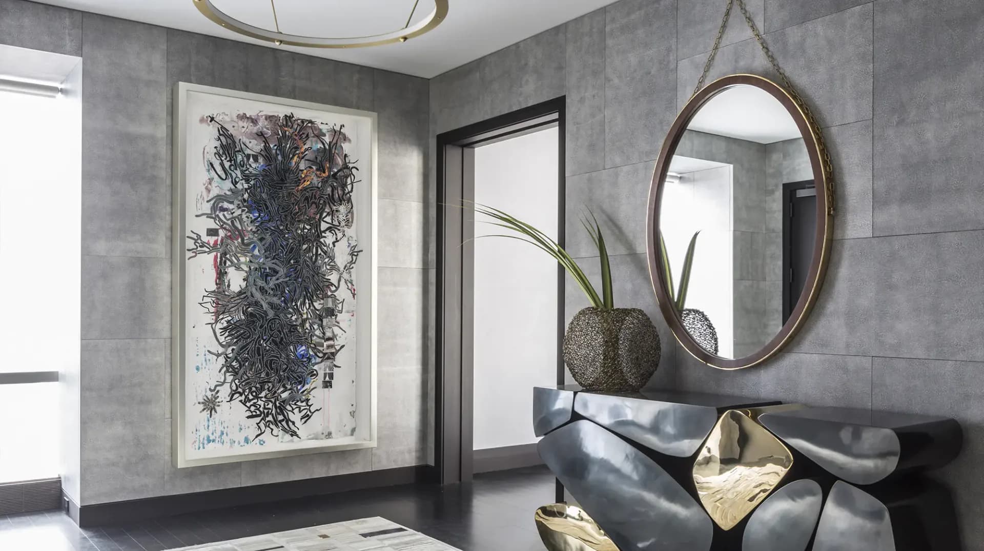 Modern entryway with gray tile walls, black-framed mirror, abstract artwork, and sculptural gold-accented seating by Jamie Drake.