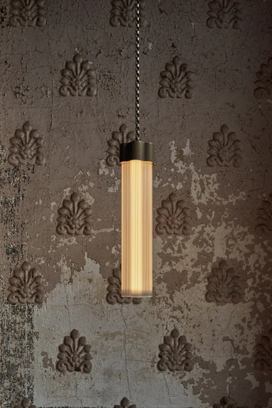 Cylindrical wooden pendant light with ribbed texture suspended against distressed ornamental wallpaper in a muted taupe palette by Jamie Gray.