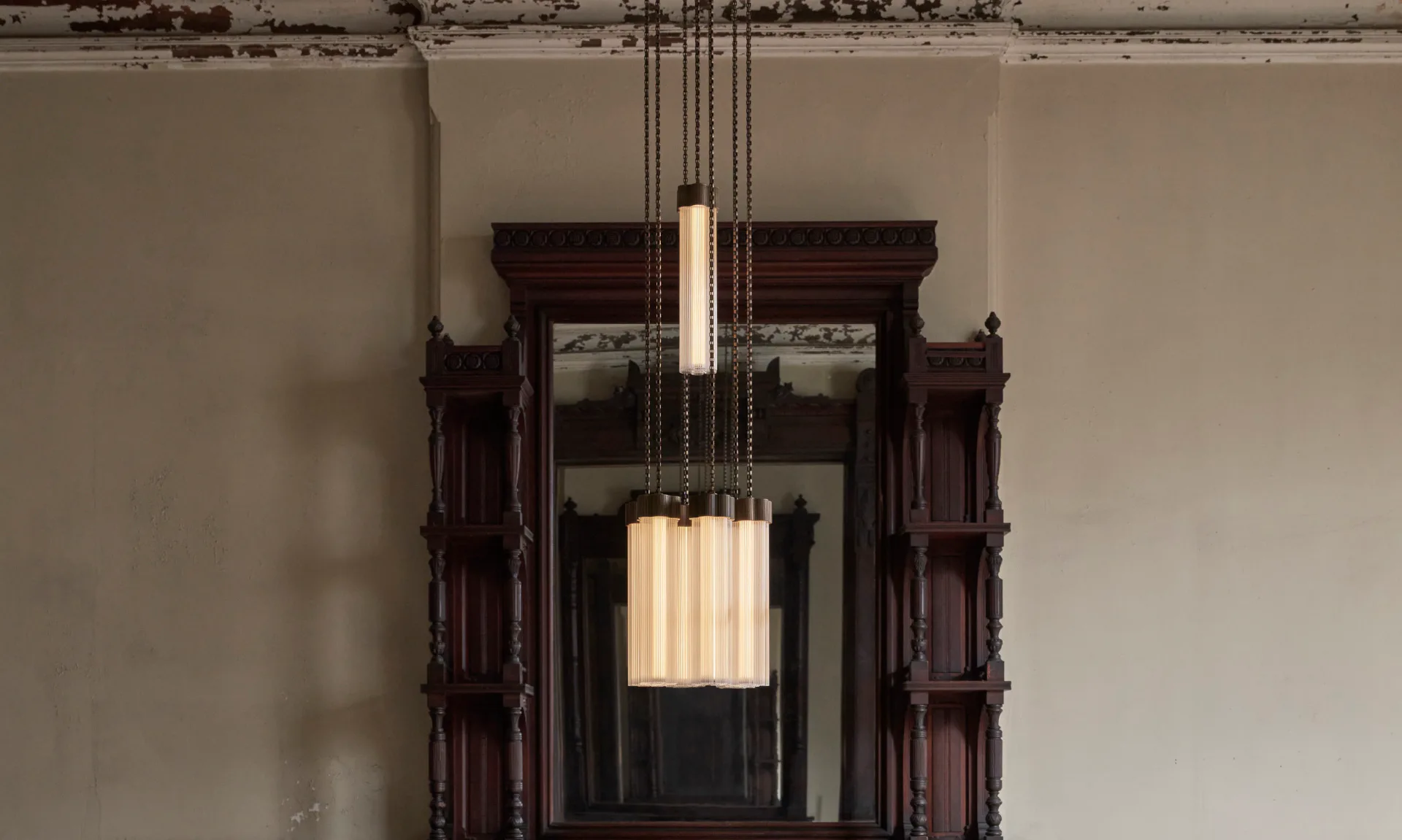 Modern pendant lighting fixture with cylindrical ribbed glass shade suspended in a dark wooden architectural doorway frame, neutral walls by Jamie Gray.