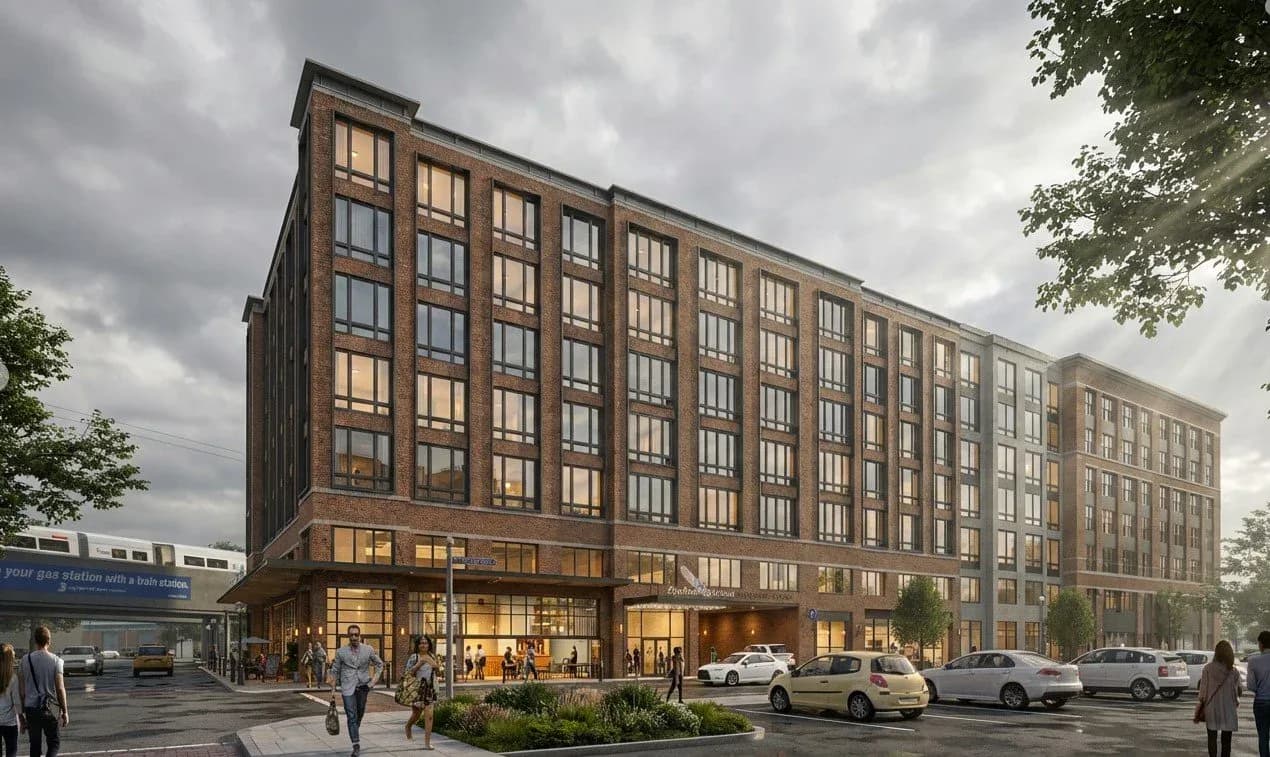 Mixed-use urban building with warm-toned brick facade, large ground-floor windows, and street-level retail space with pedestrians and parked cars by Janice Kirschenbaum.