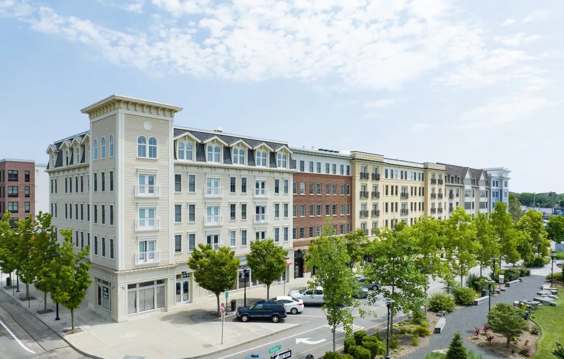 Contemporary multi-story residential building with cream and brick façades, corniced roofline, ground-floor retail, and tree-lined street frontage by Janice Kirschenbaum.