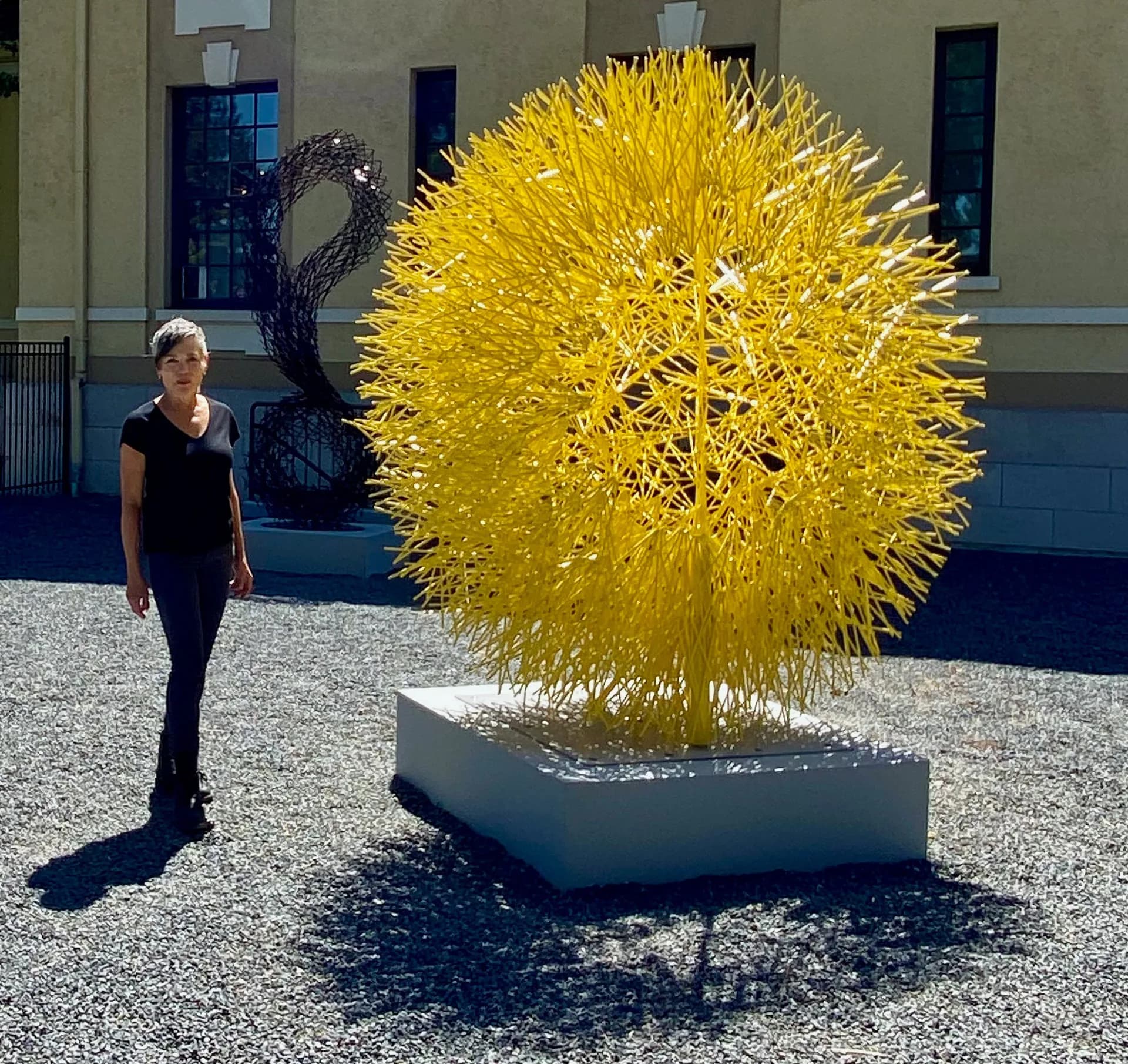 Large spherical public art installation with bright yellow spiky form on concrete plinth, architectural courtyard setting by Jann Nunn.
