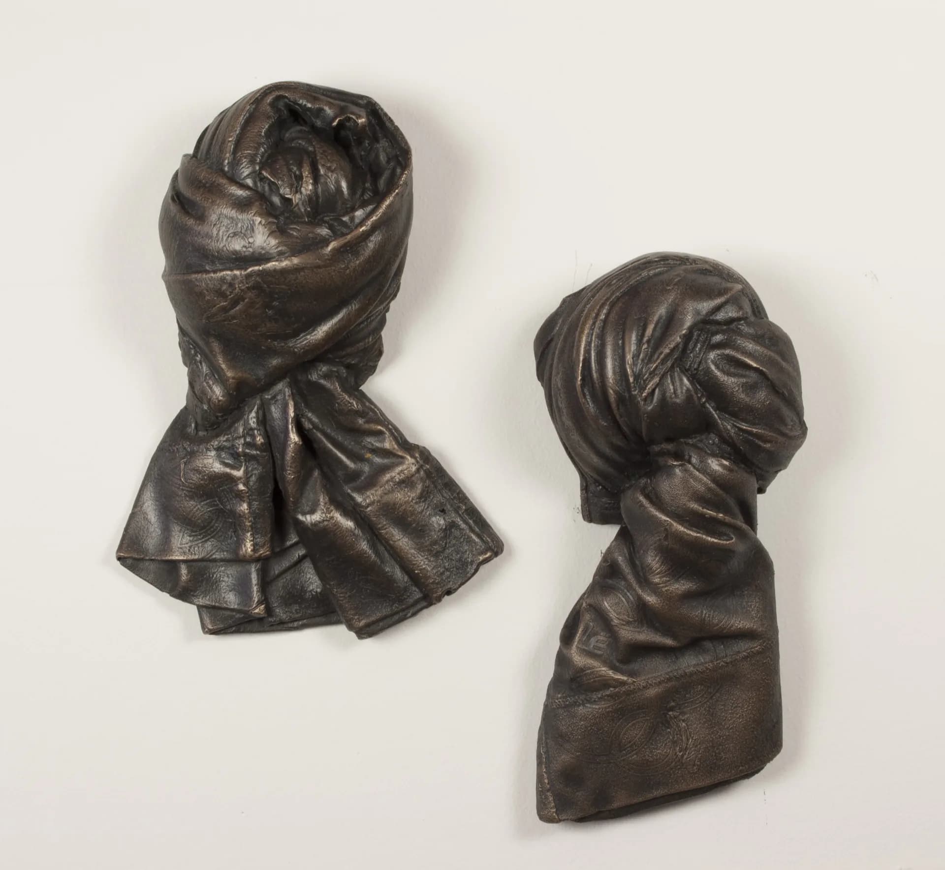 Two dark bronze sculptural busts depicting human heads and shoulders against a neutral background, by Jann Nunn.