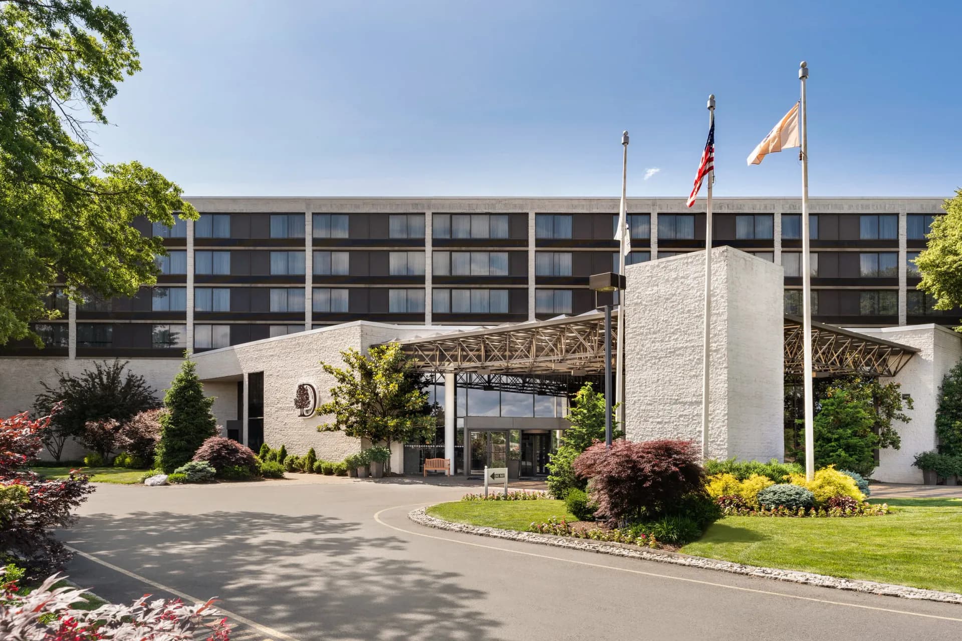 Modern hotel exterior with curved white stone facade, multi-story residential wing, manicured landscaping, and flagpoles by Jasmine Jia.