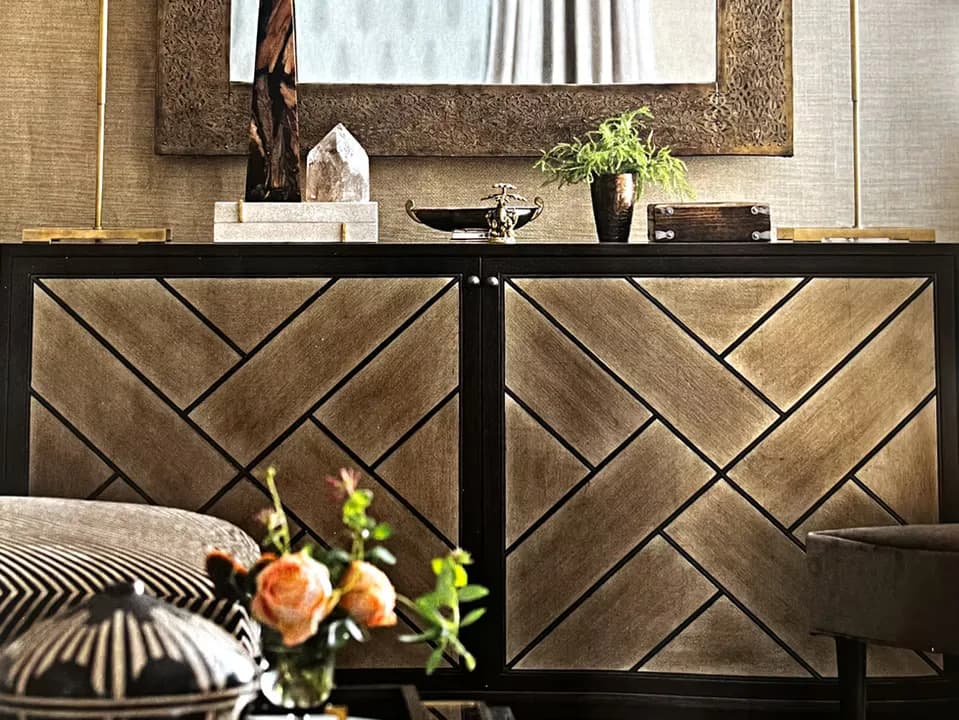 Modern bedroom interior featuring a geometric herringbone pattern headboard in warm wood tones, black metal frame, and neutral bedding with decorative pillows by Jason Fox.