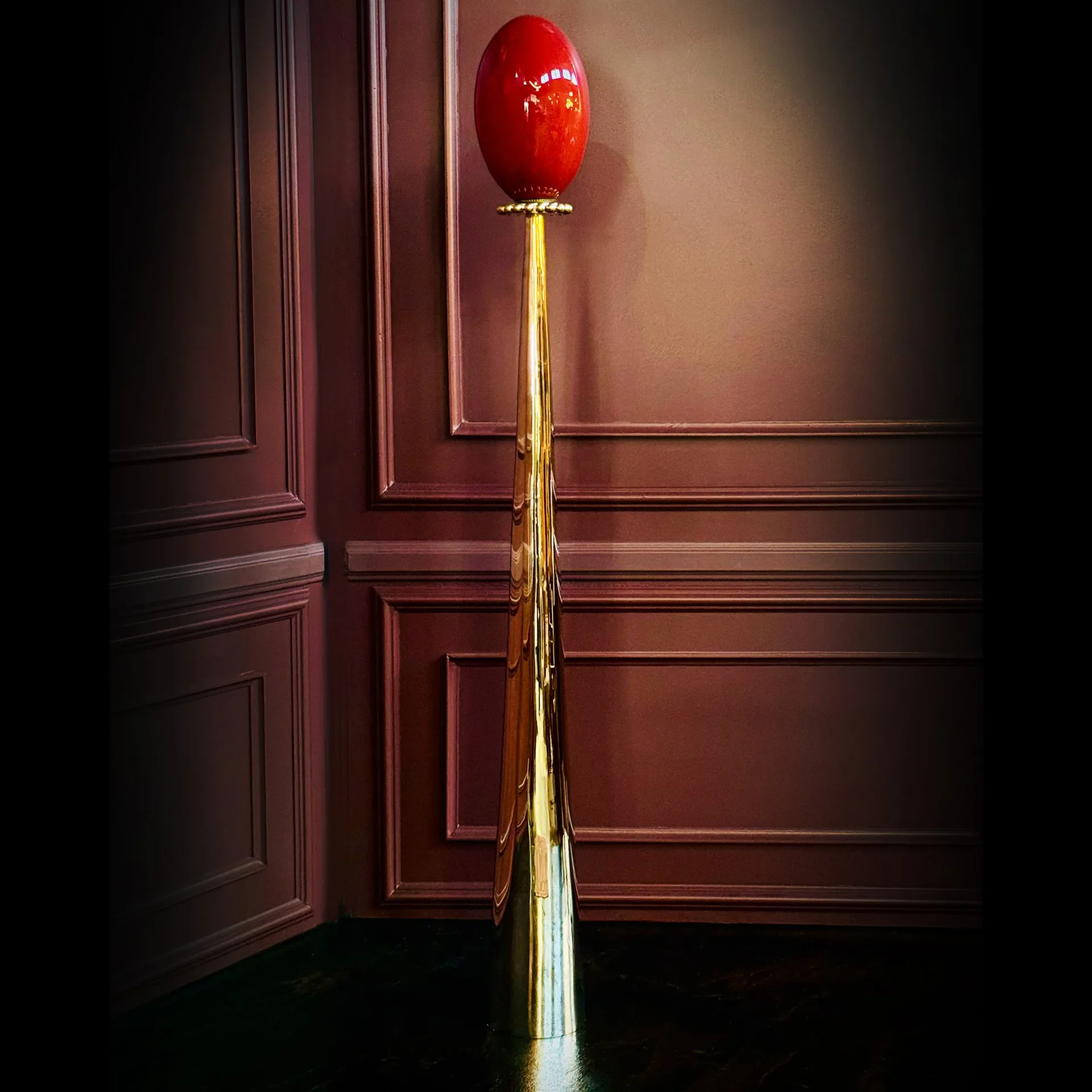 Red balloon suspended from a gold chain against burgundy paneled walls in an elegant interior installation by Jason Koharik.