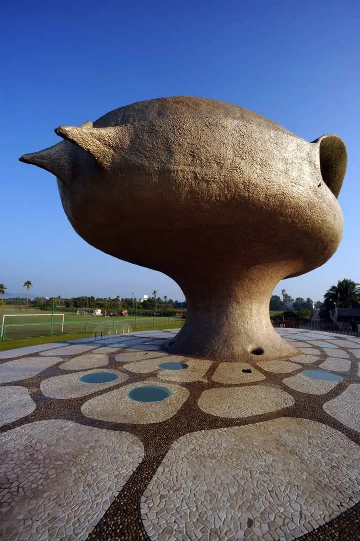 Large-scale bronze bird sculpture with geometric patterned ground featuring circles and organic forms, overlooking open fields by Javier Senosiain.