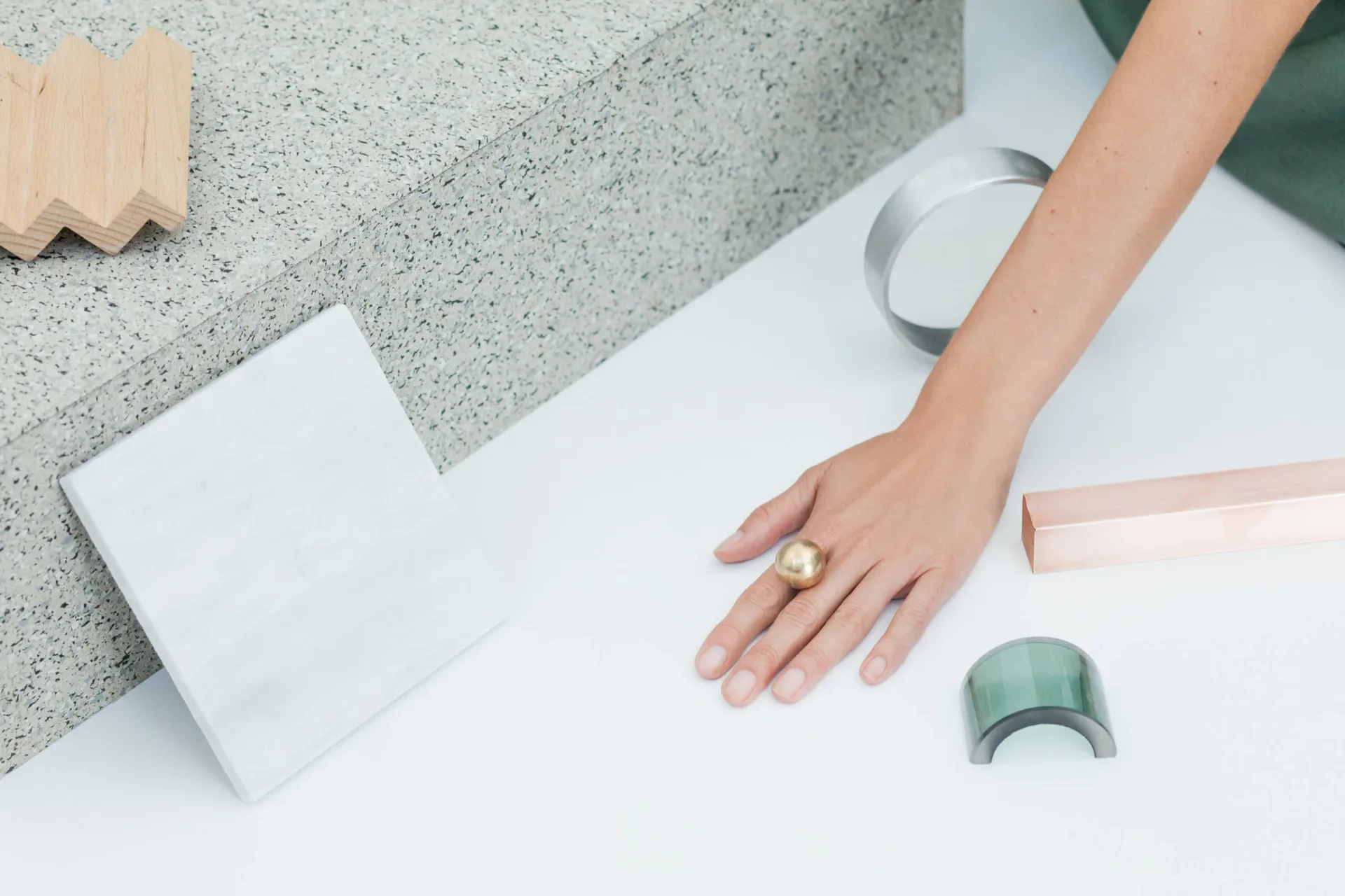 Minimalist product styling featuring concrete and terrazzo samples with tape and natural materials on white surface by Jean Lee.