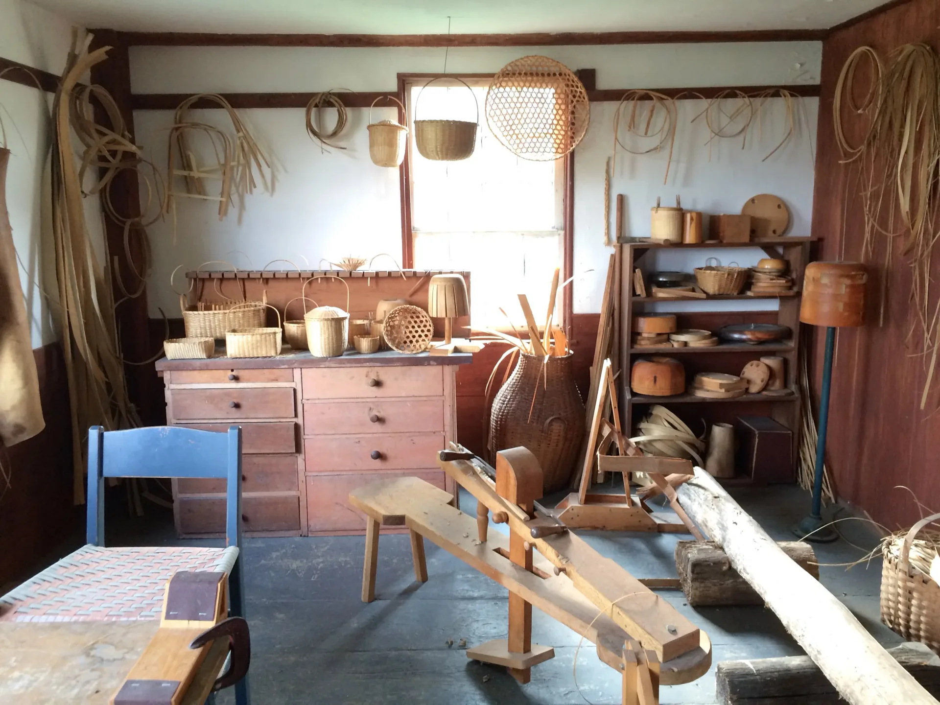 Rustic interior space with wooden furniture, clay vessels, and woven baskets arranged on shelves and surfaces, showcasing warm earthy tones and traditional craftsmanship by Jean Lee.