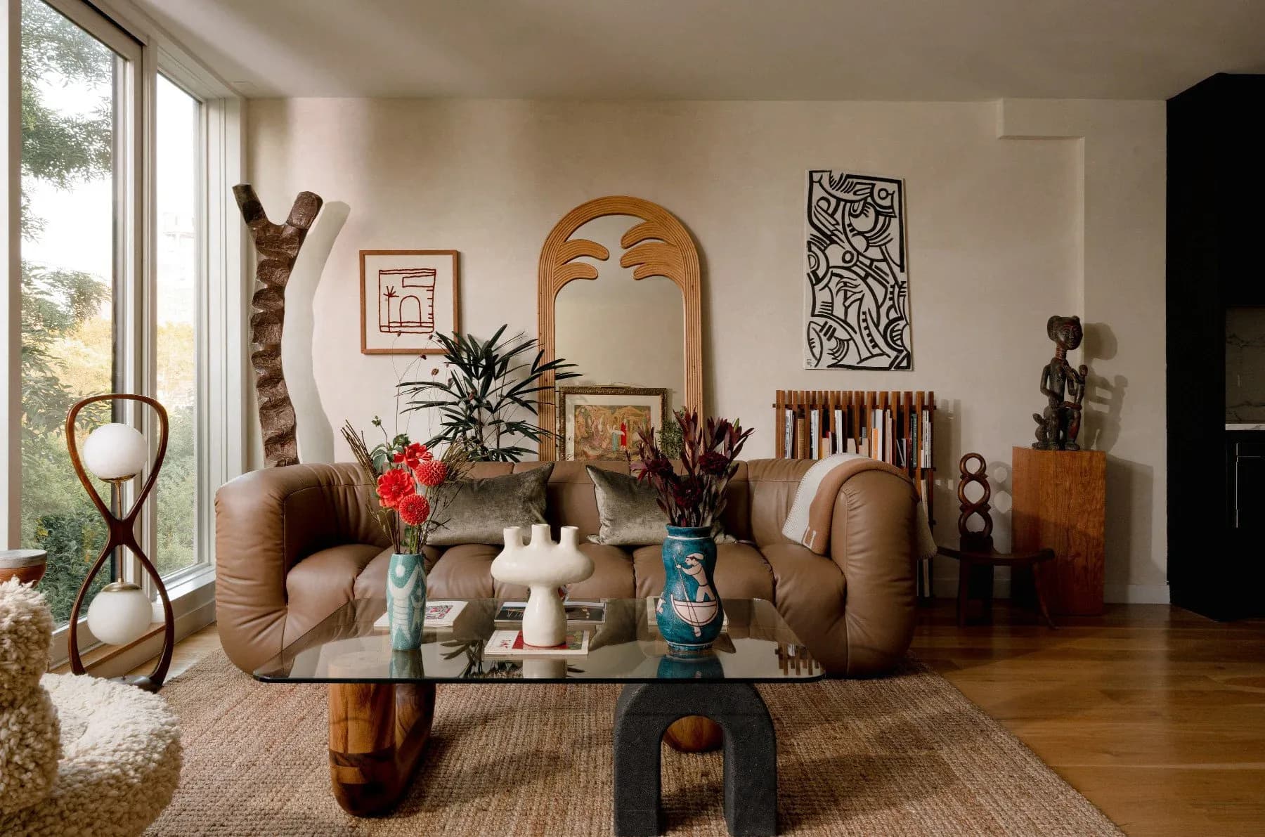 Warm-toned living room with curved caramel leather seating, sculptural wooden coffee table, curated art collection, and lush plant styling by Jean Parker.