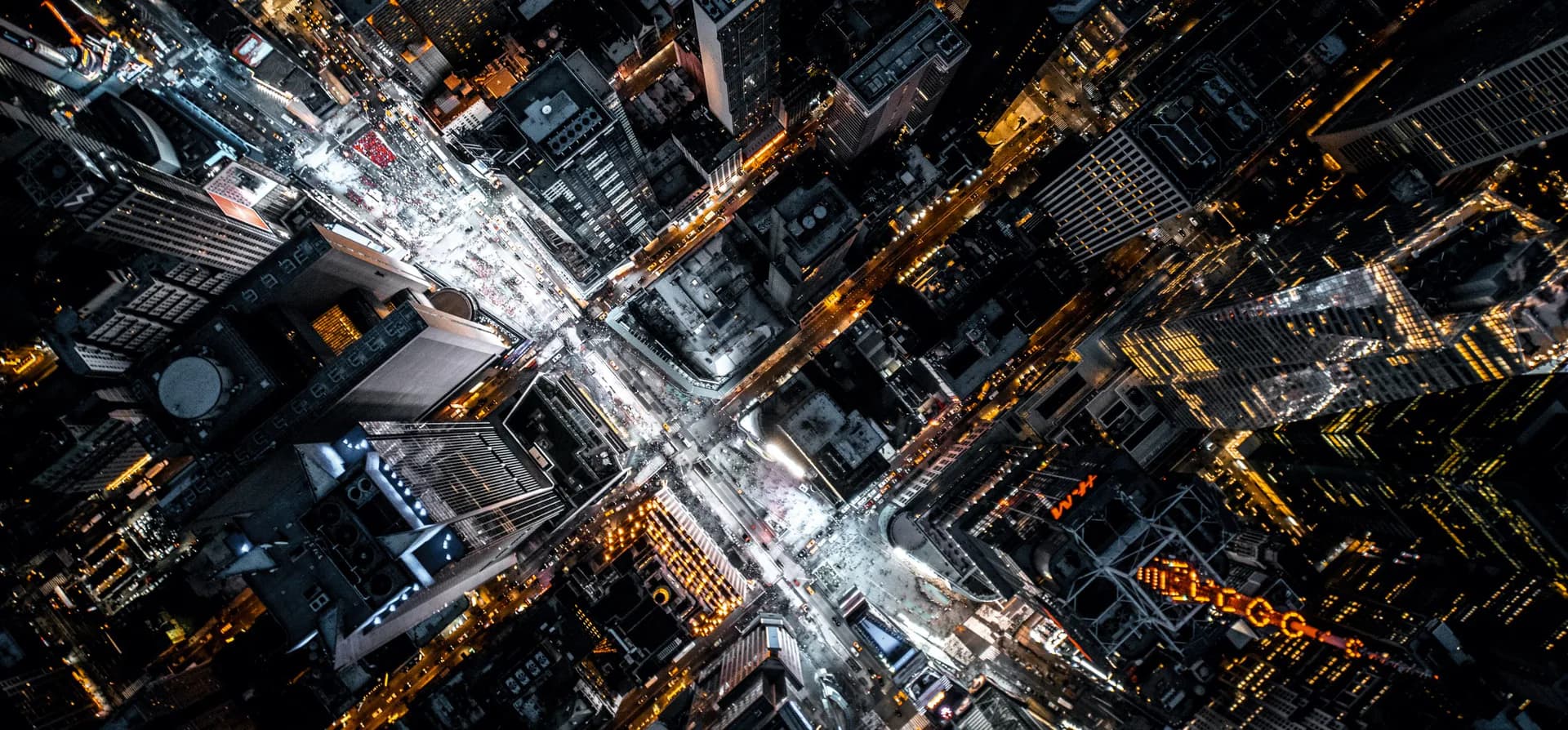 Aerial nighttime view of Manhattan street intersection with illuminated buildings and white street lights creating a dramatic urban grid pattern by Jean Sundin.