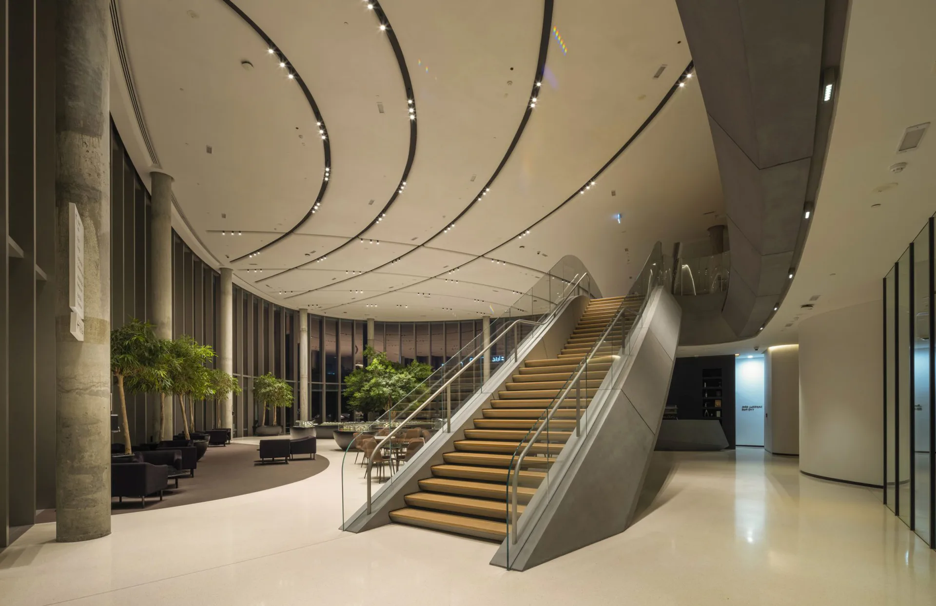 Modern lobby with curved ceiling details, central staircase with golden treads, polished floors, and natural lighting by Jean Sundin.