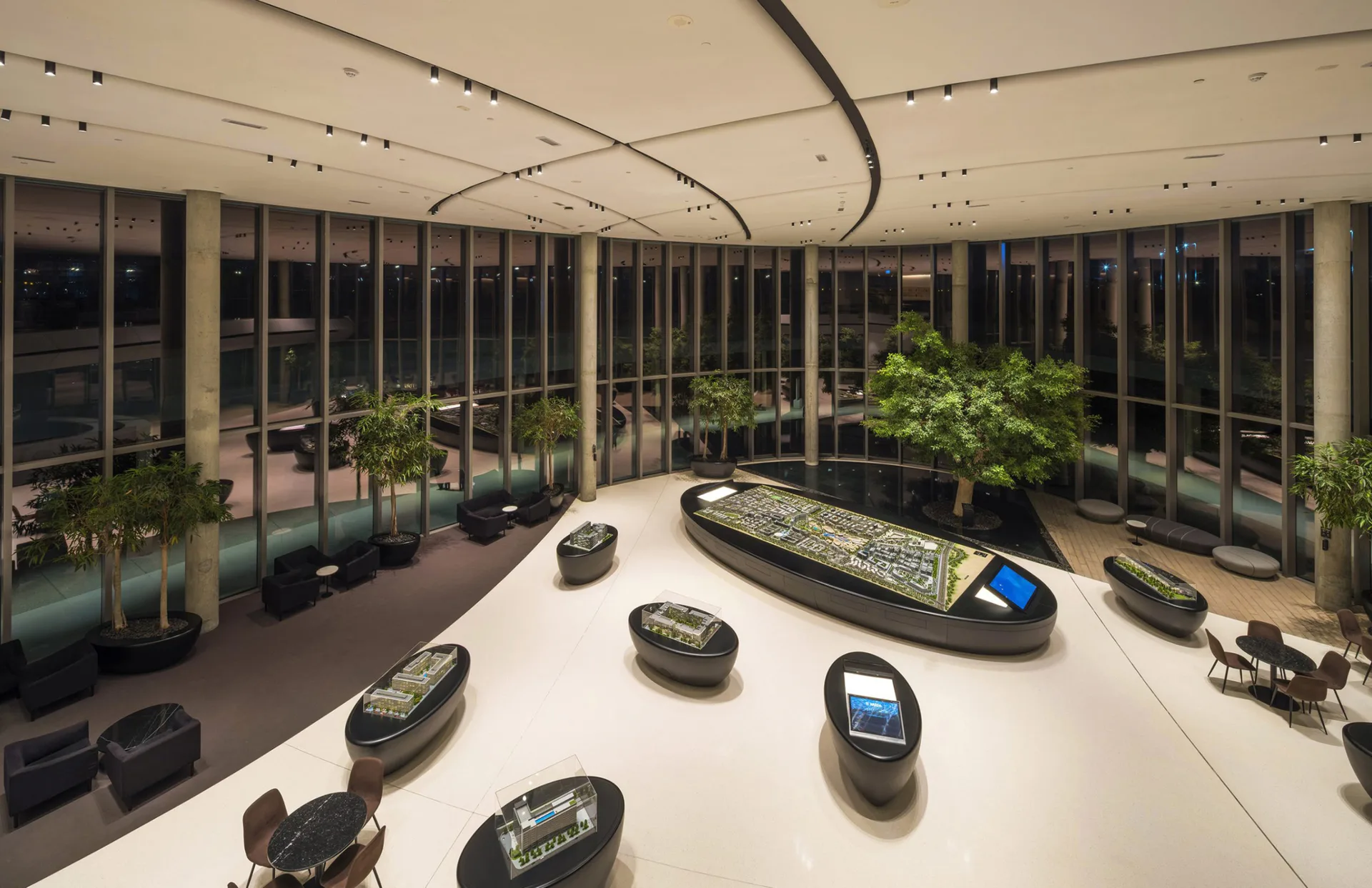 Modern curved showroom with floor-to-ceiling windows, white ceiling with integrated lighting, potted plants, and sculptural boat displays on a white floor by Jean Sundin.