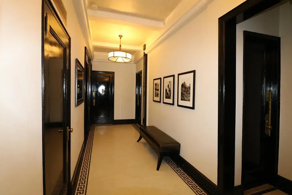 A modern hallway with cream-colored walls, black-trimmed doors, geometric patterned flooring, and framed artwork, designed by Jeanne Isaacson.