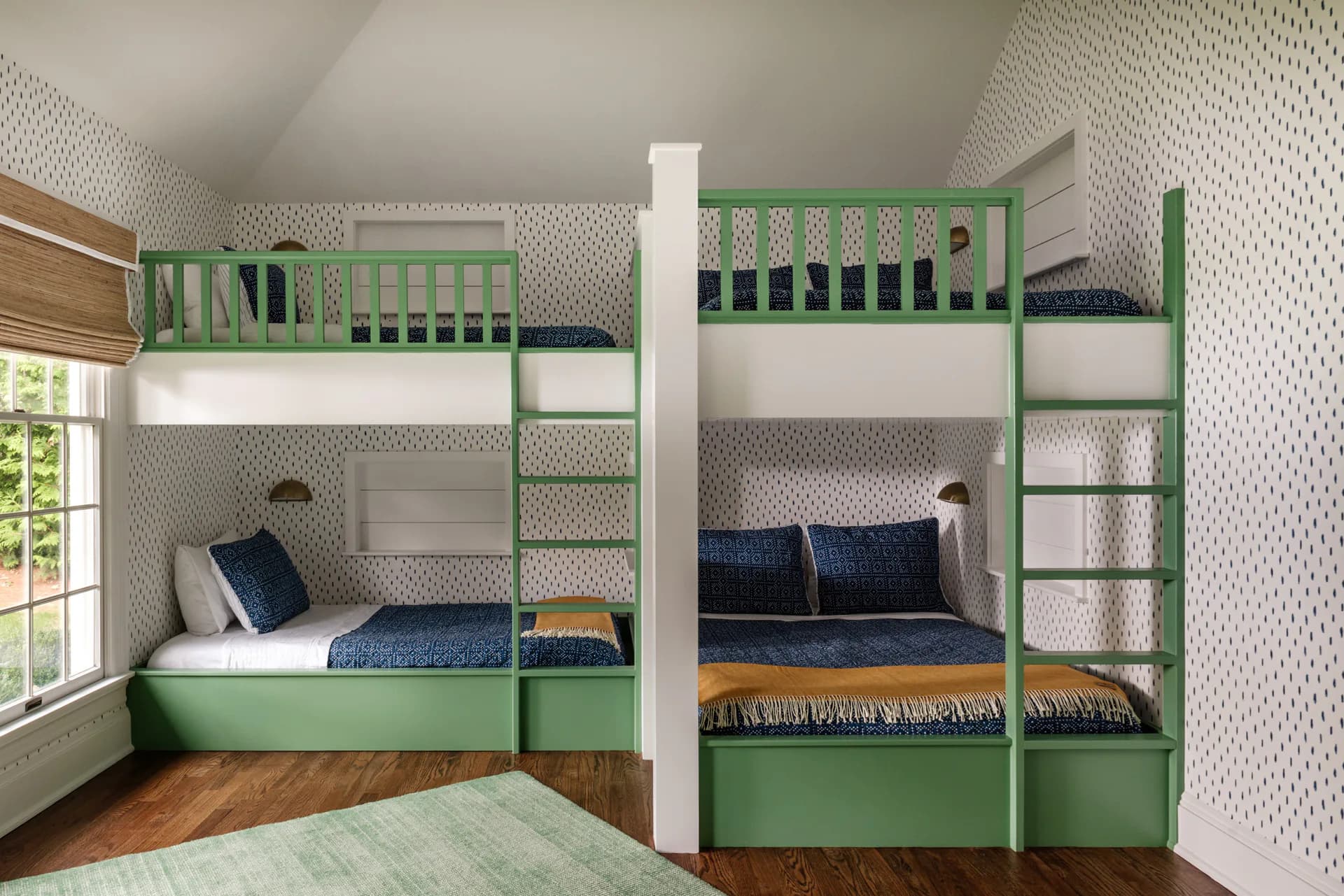 A children's bedroom with custom green and white bunk bed furniture featuring built-in storage, patterned wallpaper, and hardwood flooring, designed by Jen DeLalio.