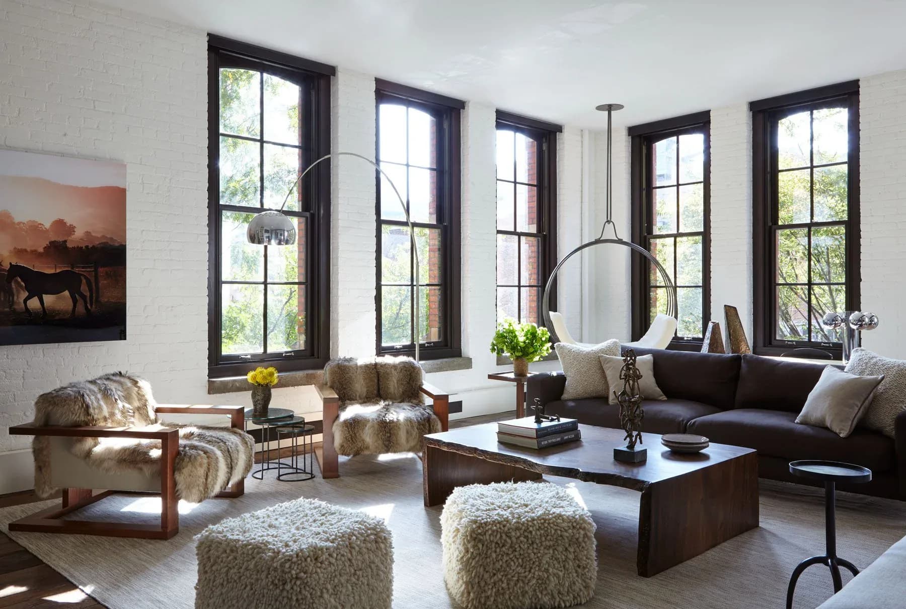 Modern living room with black-framed windows, neutral furnishings, and a suspended circular pendant light, designed by Jena White.