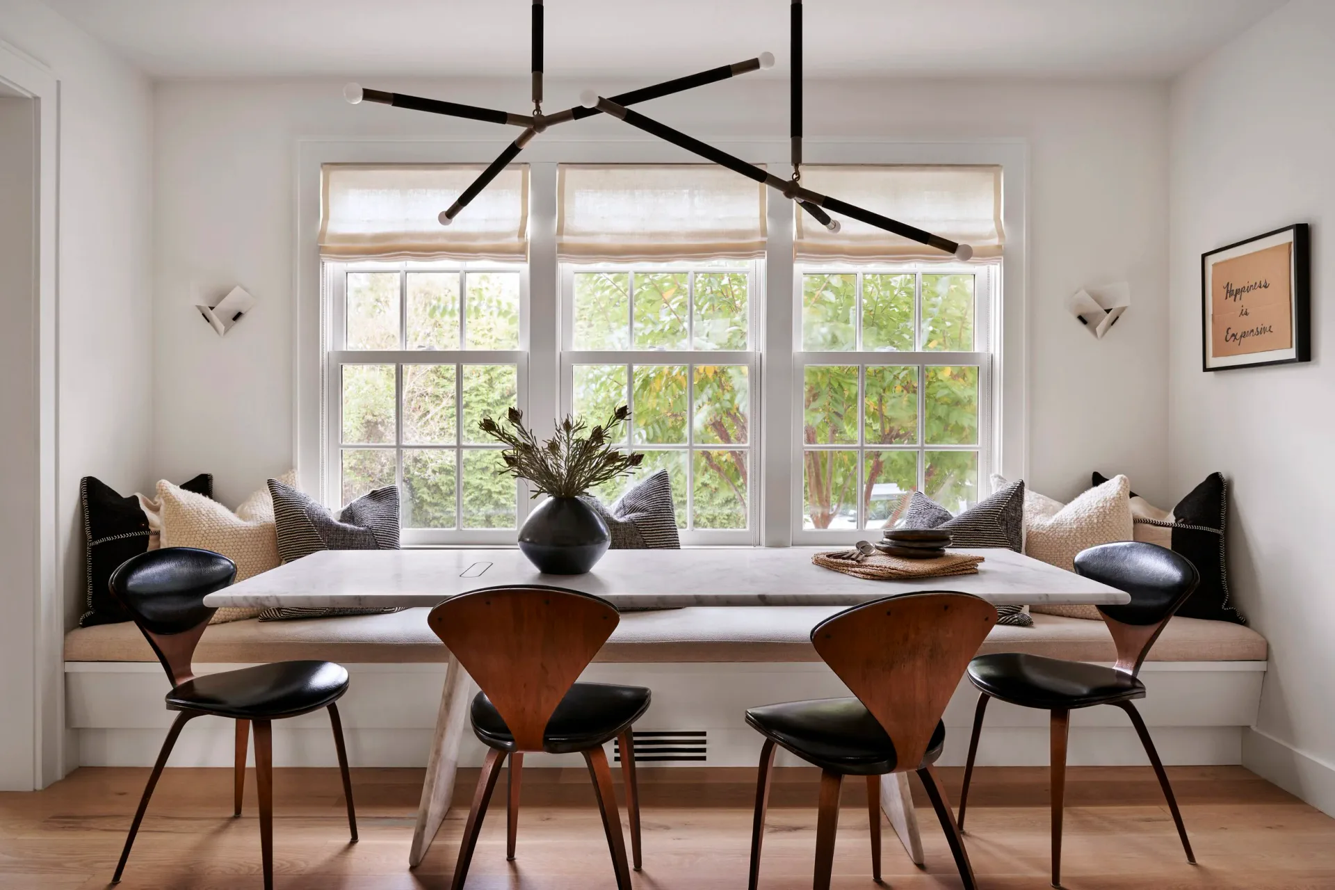 Bright dining nook with built-in window seating, mid-century modern chairs, pendant lighting, and natural wood accents by Jena White.